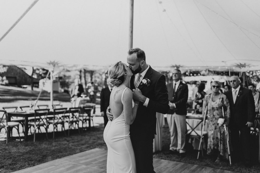 Couple dances in center of tent reception while wedding party and guests observe from perimeter.