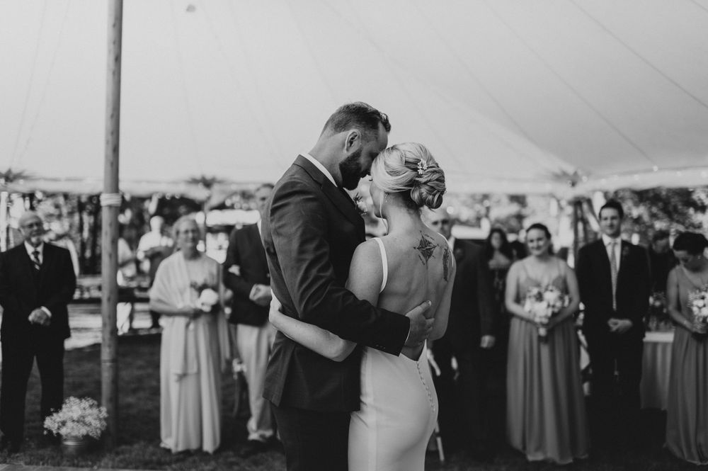 Couple shares their first dance under a white tent at an outdoor wedding reception.