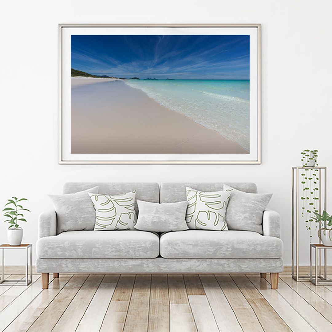 Framed coastal artwork showing pristine white beach and turquoise waters above a modern grey sofa.
