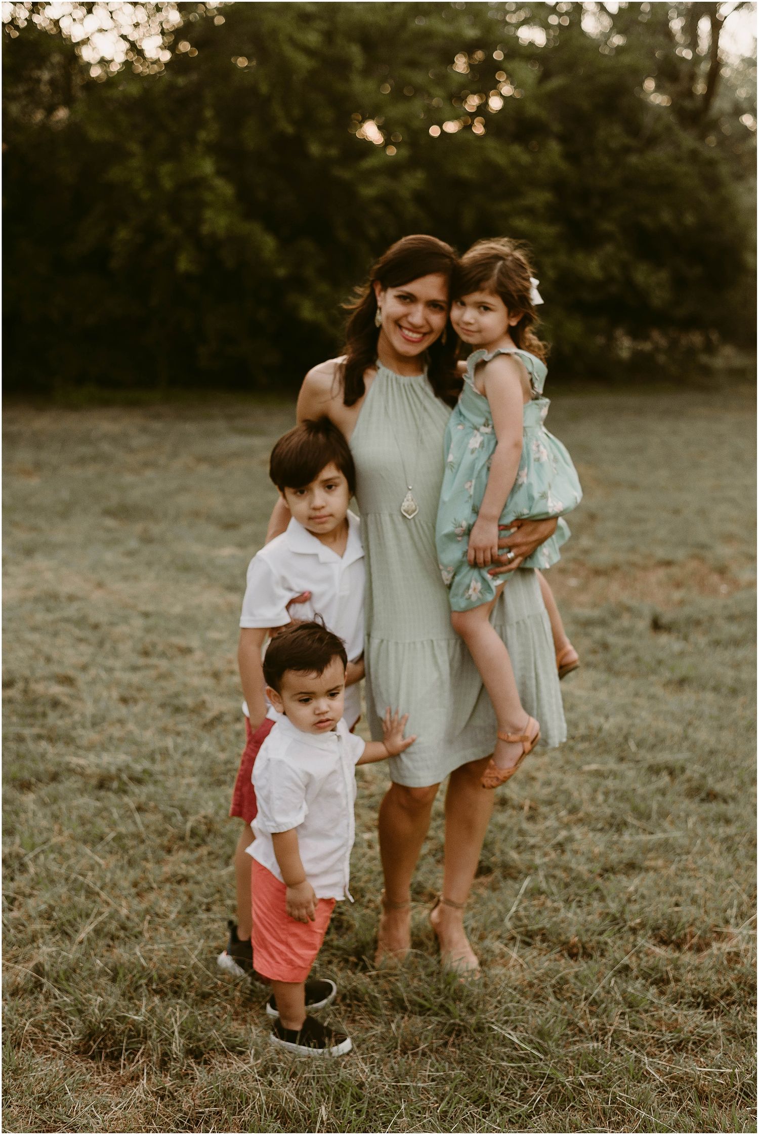 Three children pose with their parent in a field wearing coordinated outfits during golden hour.