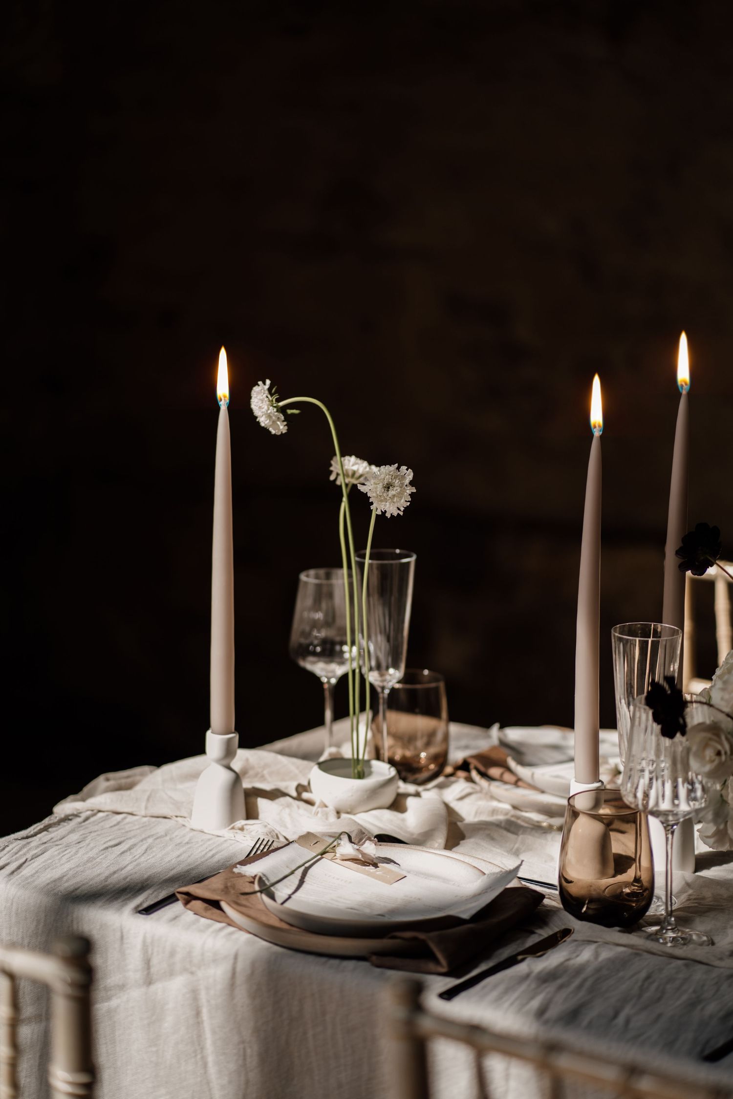 Wedding table with beige candles and glasses on a cream table cloth. A close up photograph with black in the background.