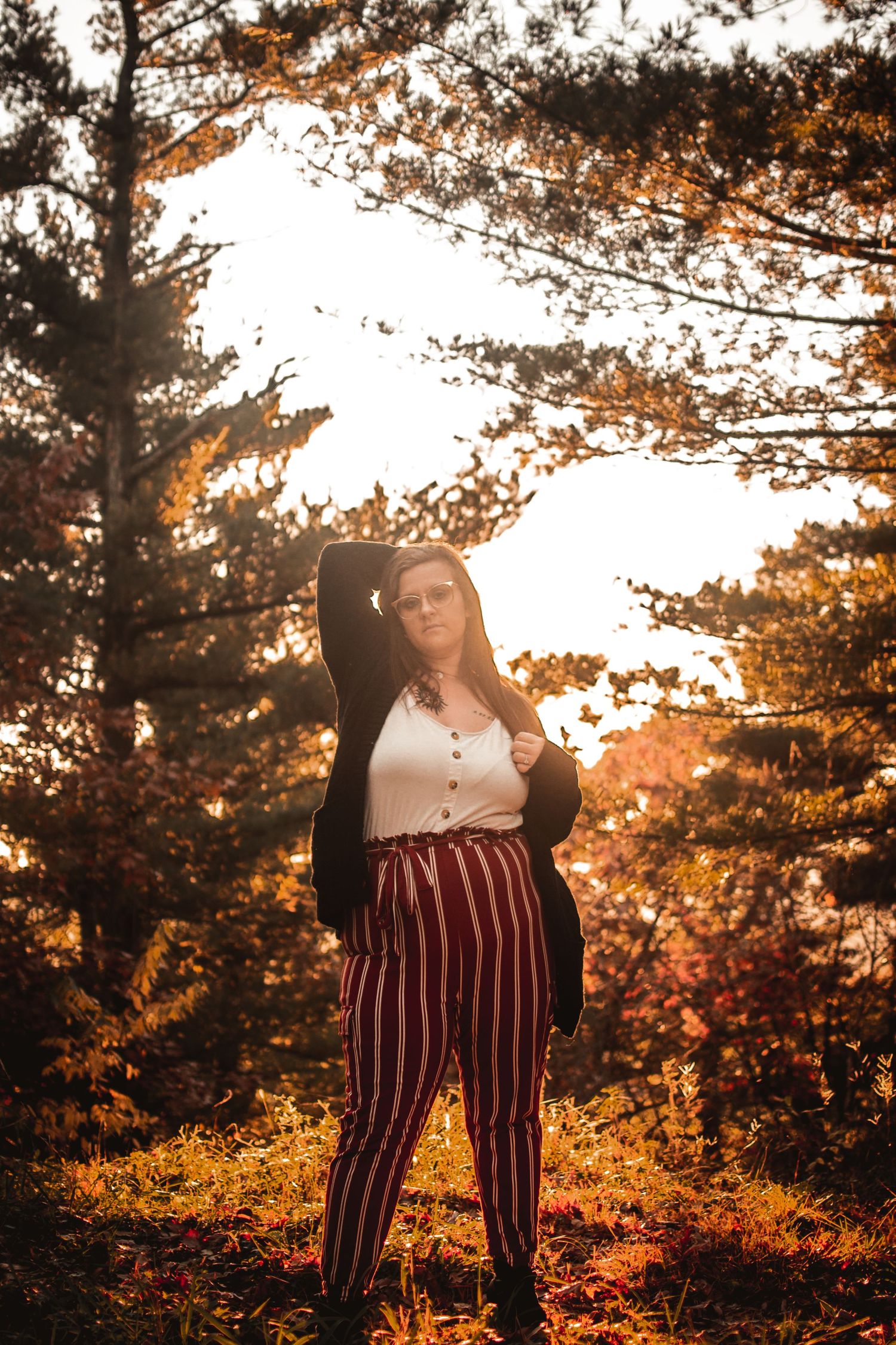 Person in striped pants poses dramatically against golden sunset in autumn forest.