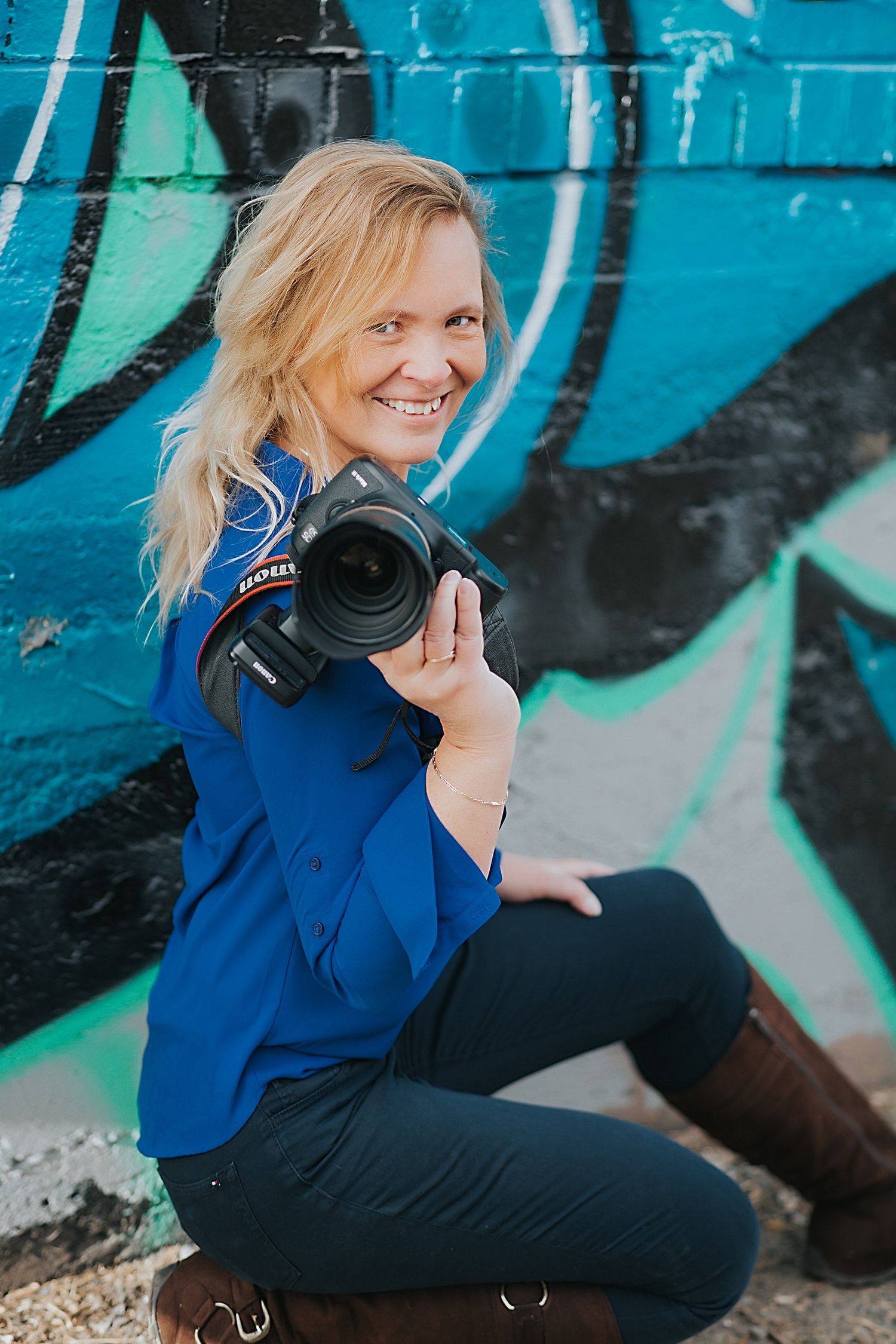 A photographer in blue crouches near a turquoise wall with graffiti art.
