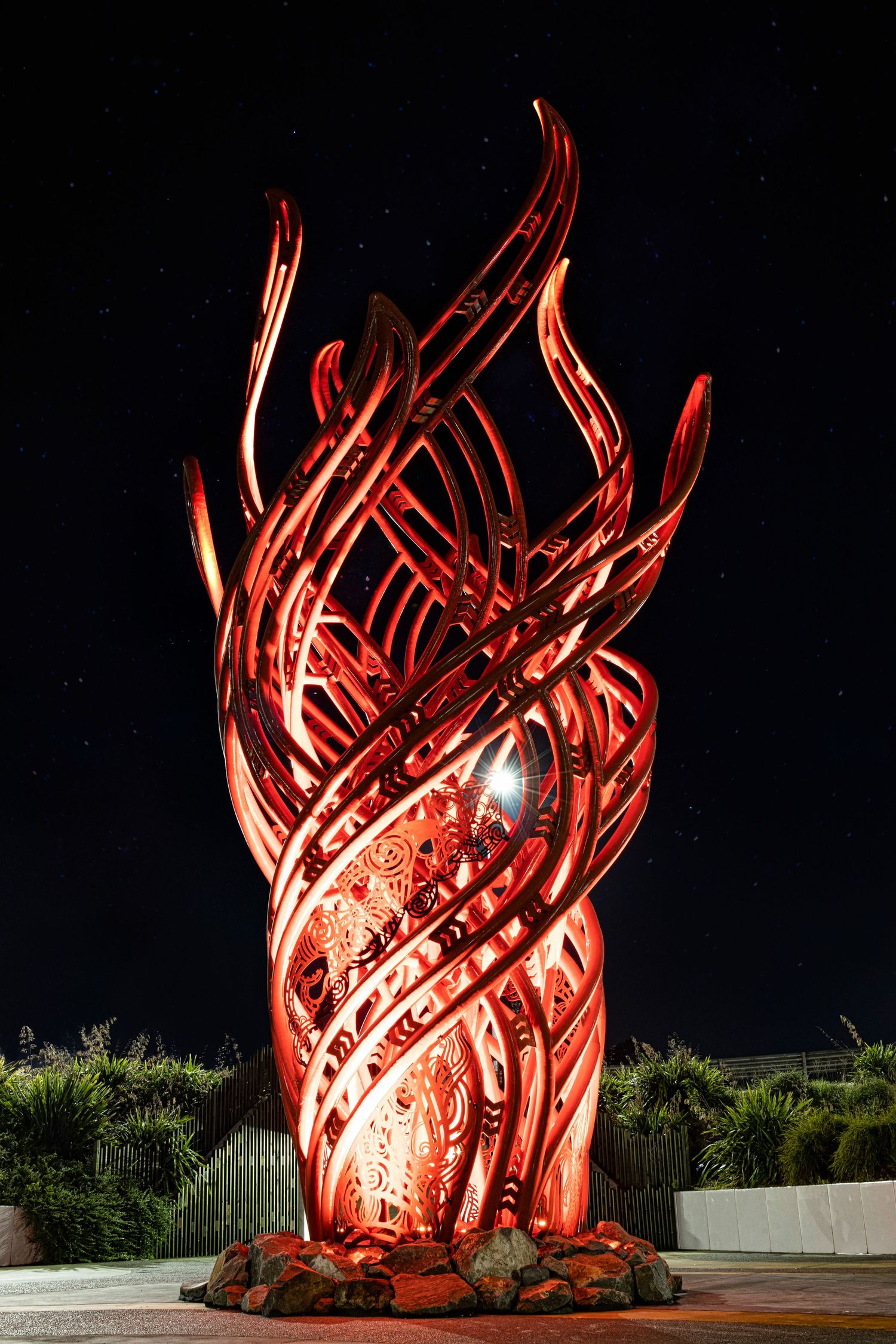 A blazing red sculpture twists skyward like flames, lighting the night with bold form and energy.