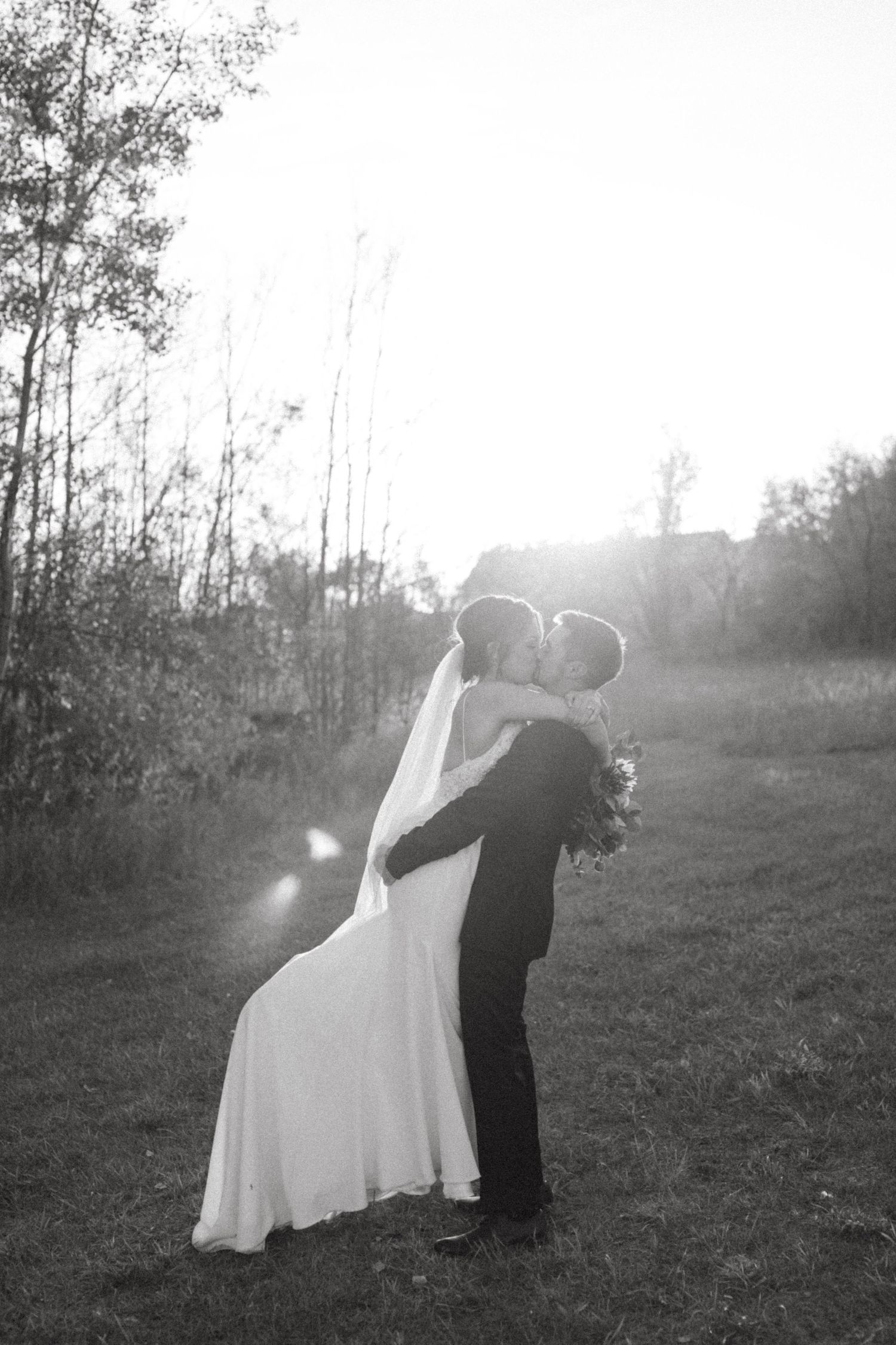 Black and white silhouette of newlyweds embracing in a field at sunset.