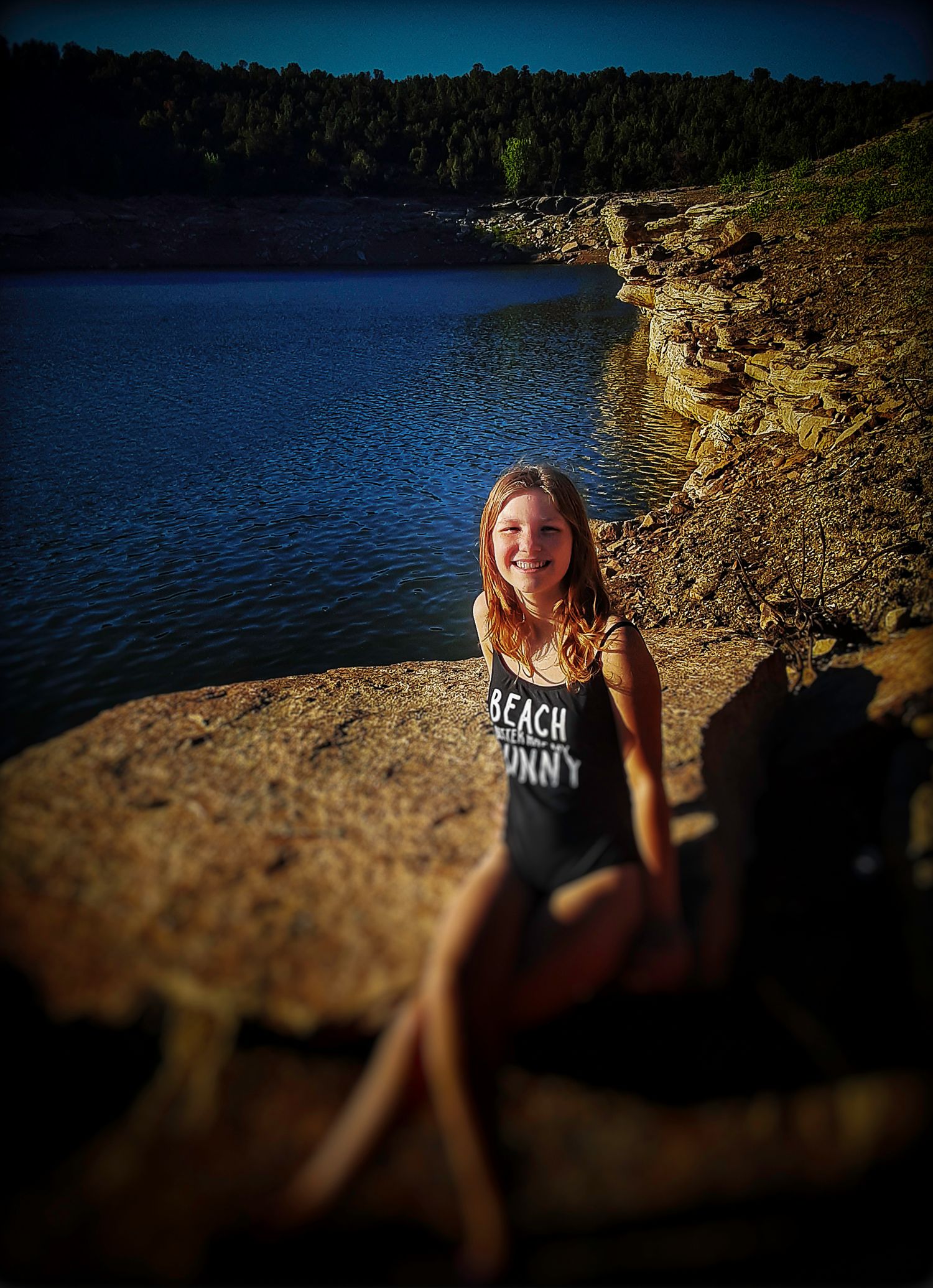 Someone sitting on rocky cliffs overlooking a scenic lake surrounded by forest.