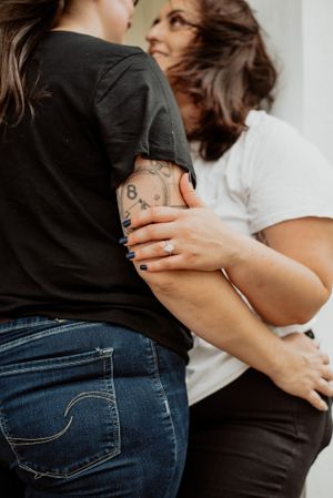Close-up of tattooed arms embracing in casual clothing against a white wall.