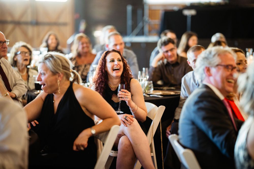 Candid shot of wedding reception guests laughing and enjoying celebration at indoor venue.
