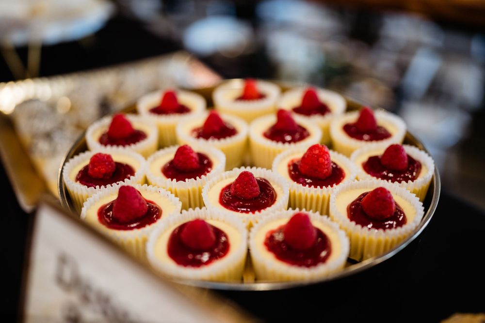 Plate of mini cheesecakes topped with fresh red raspberries arranged in neat rows.