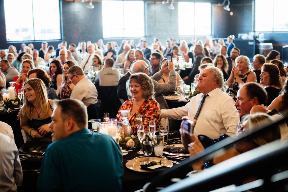 Large group of wedding guests celebrating and dining together in a dimly lit reception venue.