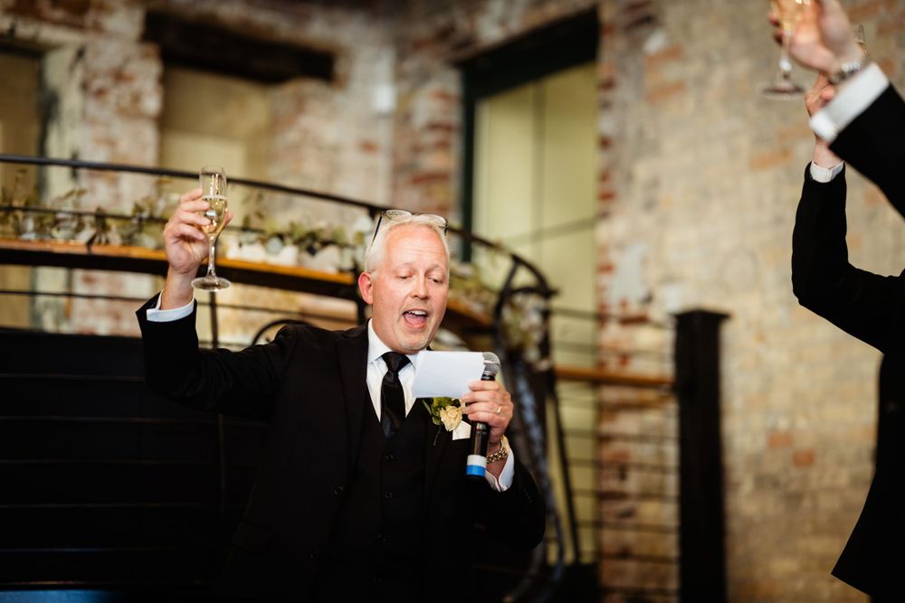 Guest raises glass during toast at wedding reception in rustic brick venue.