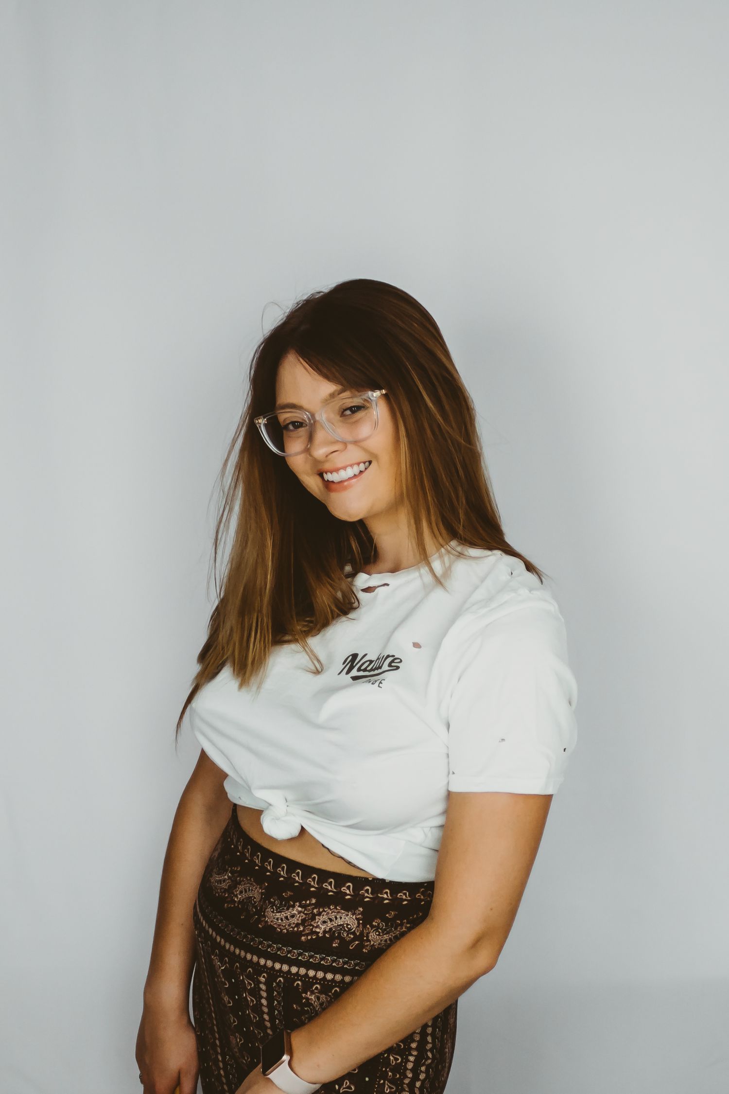 Woman in a white crop top and patterned skirt poses against a grey backdrop.