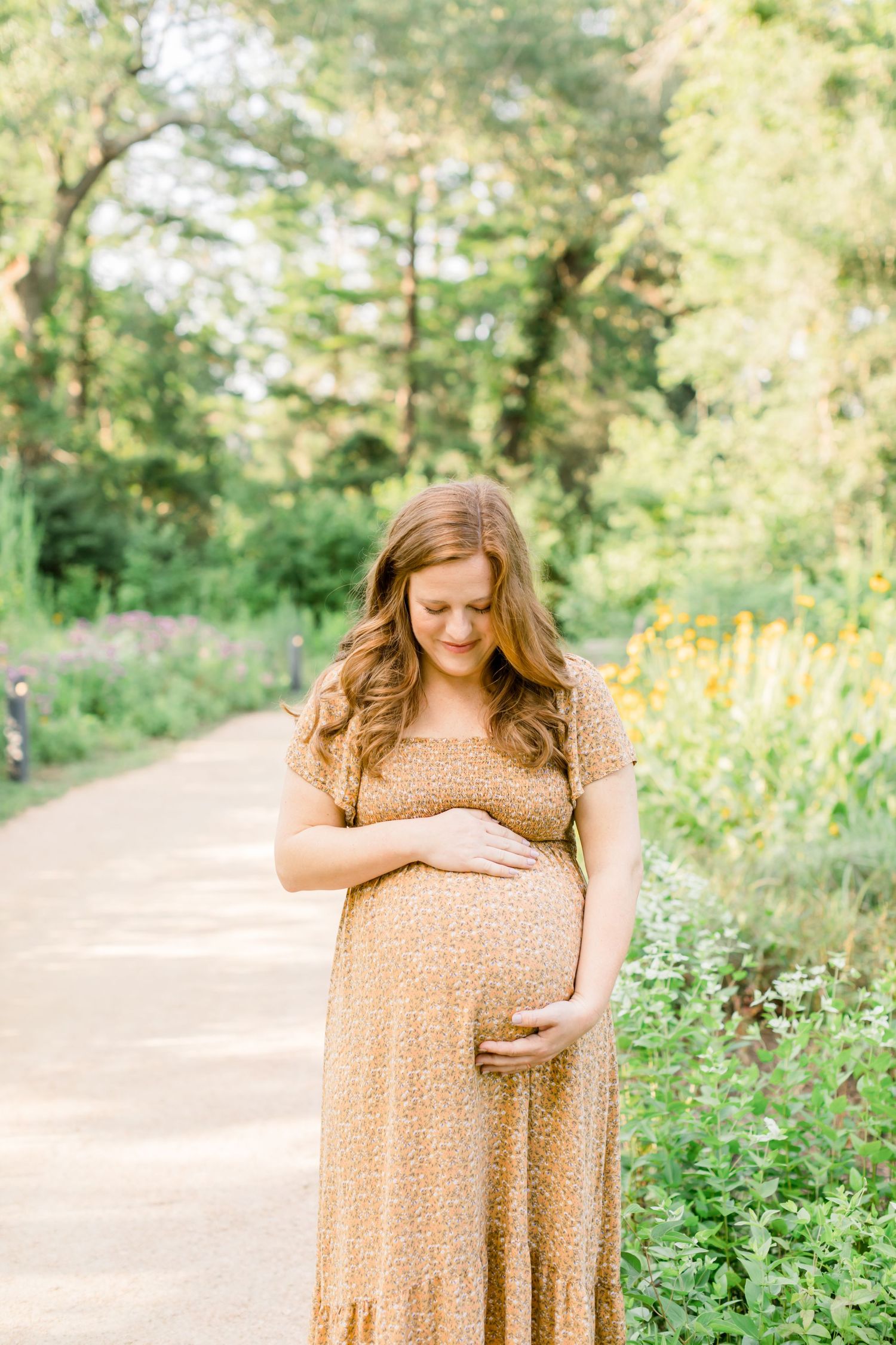 A person in a flowing tan dress stands on a peaceful garden path amidst greenery.