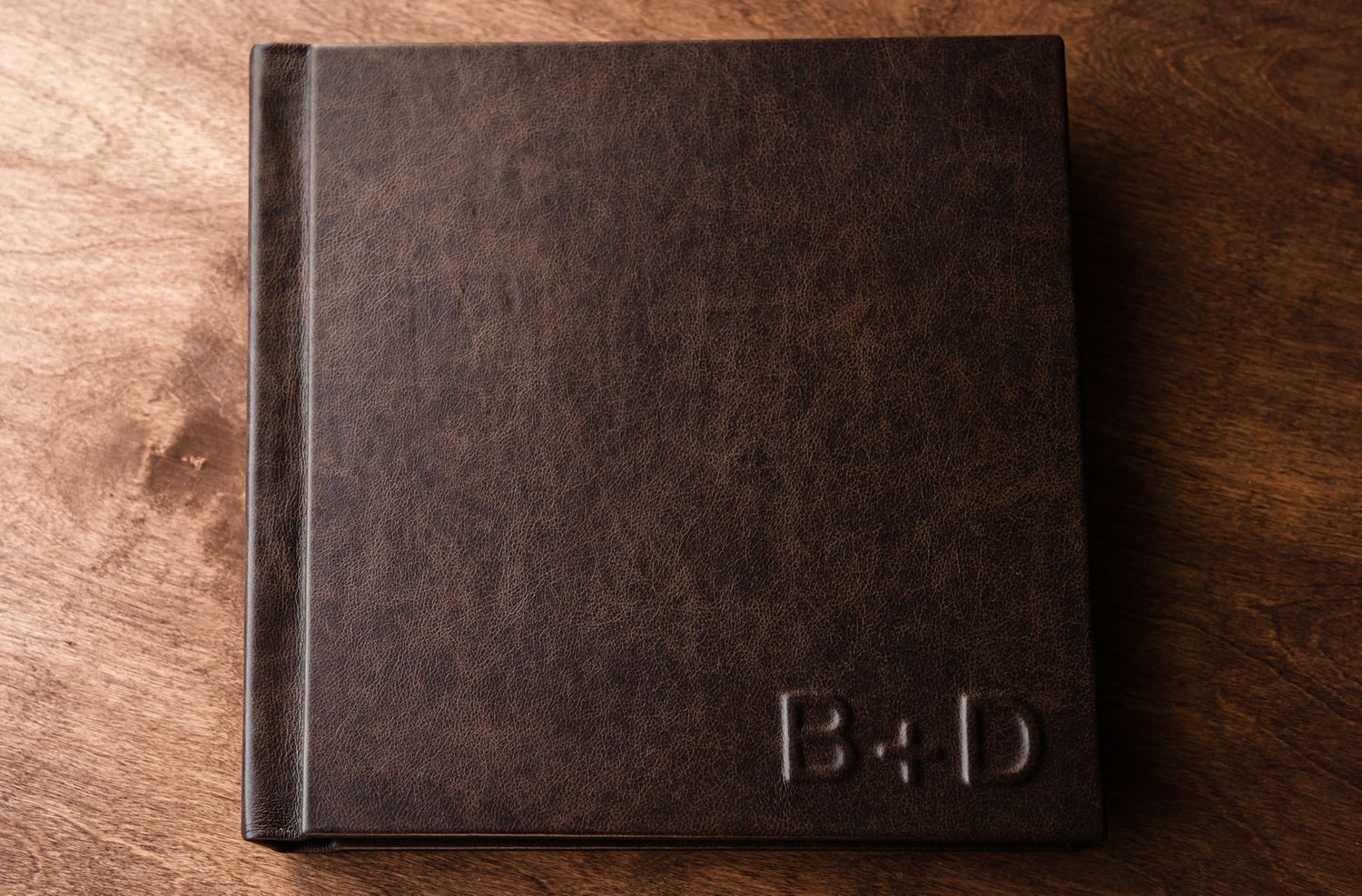 Dark leather photo album displayed on wooden surface with dramatic lighting.