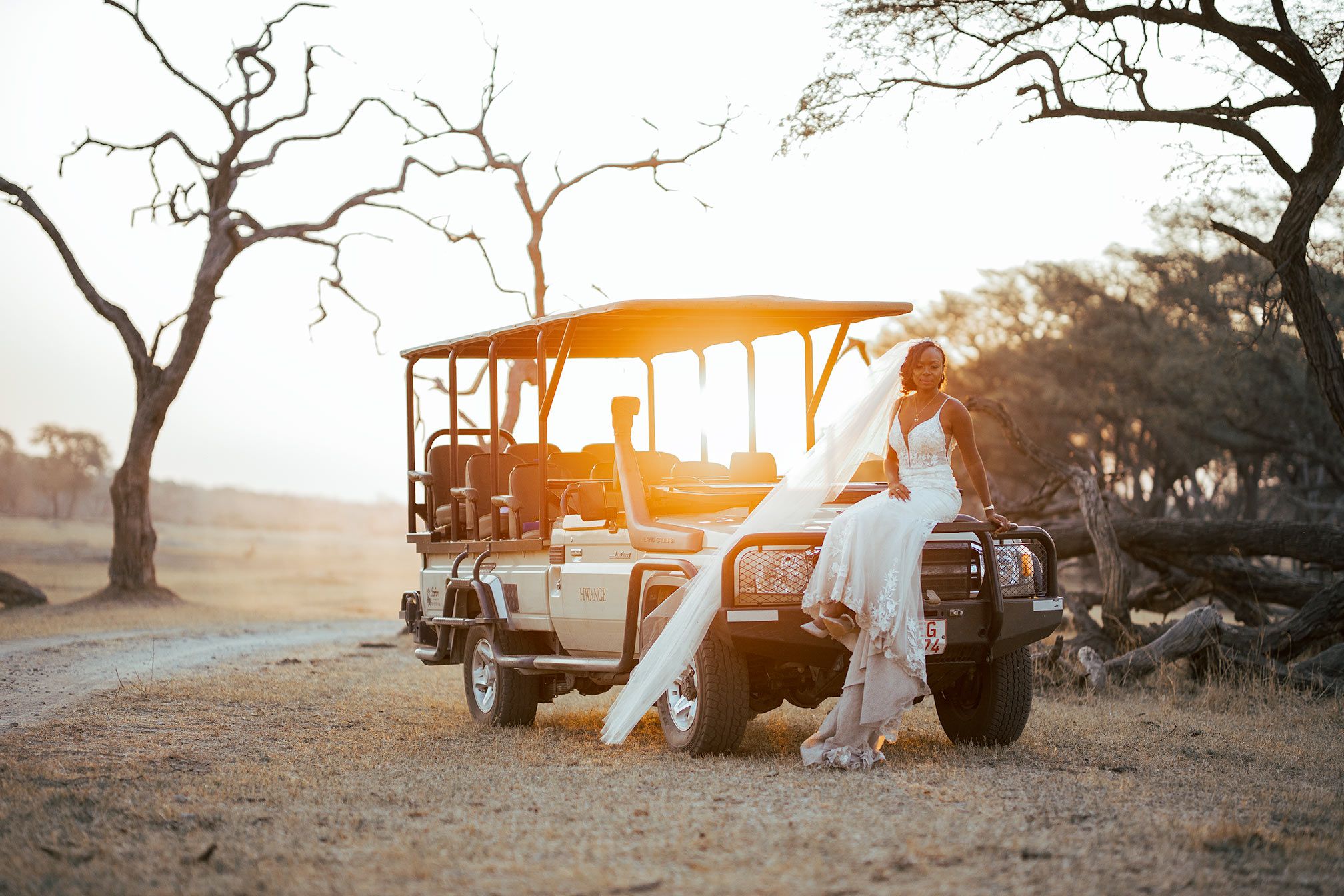 A dreamy sunset photo with a safari vehicle and flowing white dress against a golden sky.