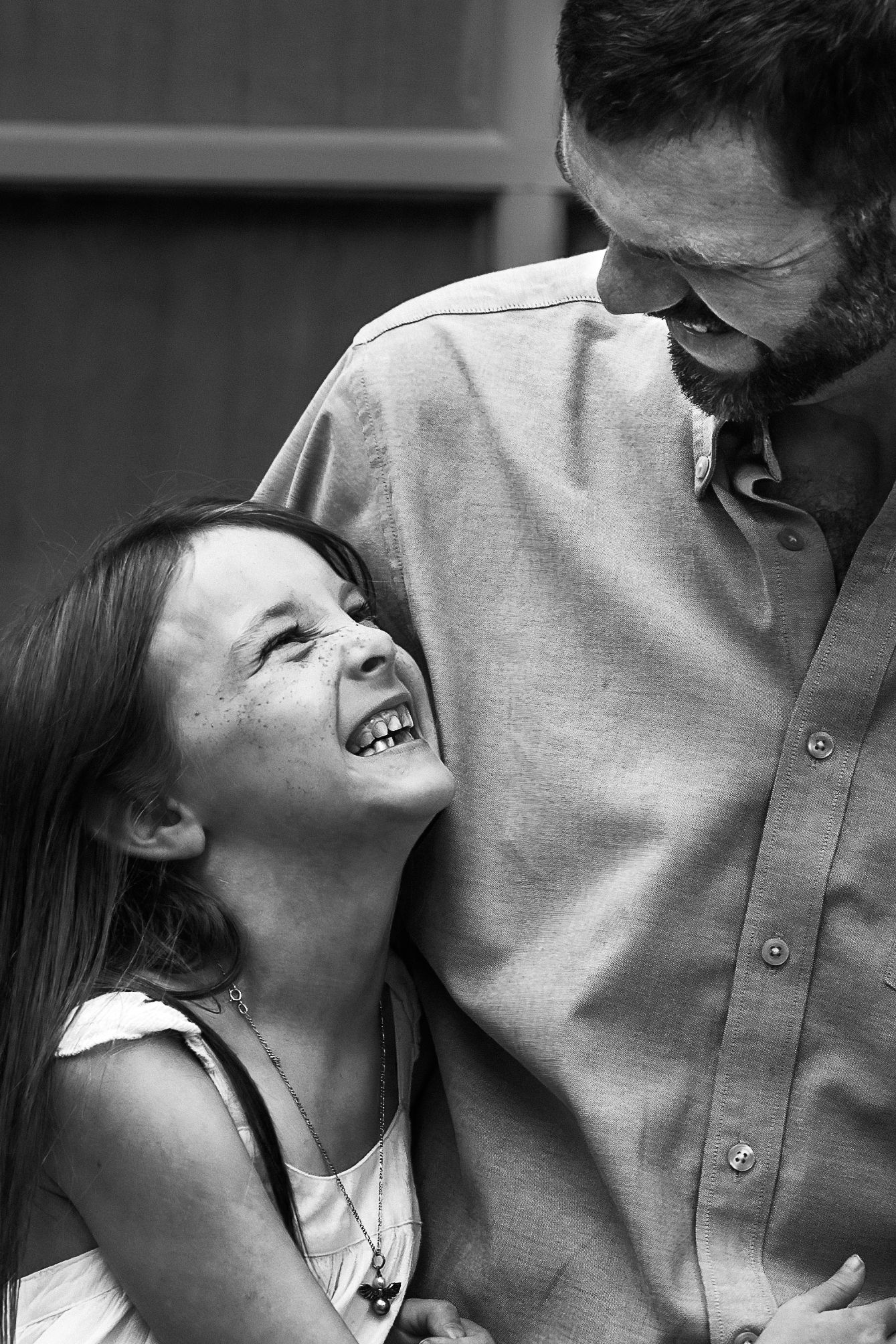 a black and white portrait of a young girl laughing while she looks up at her father
