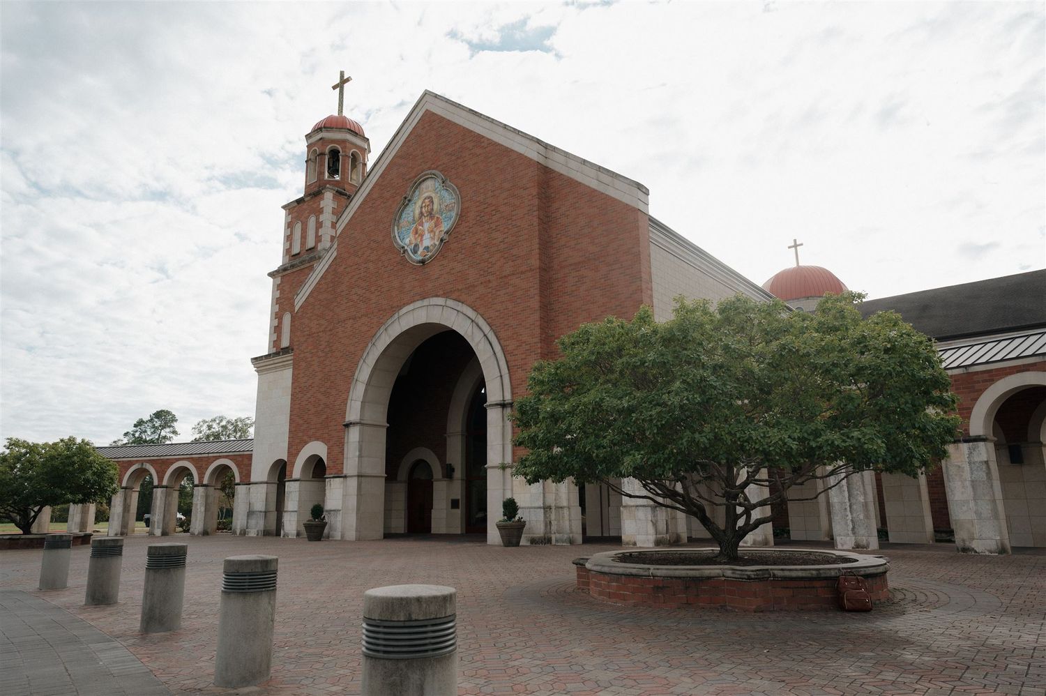 Brick church facade with arched entrance, bell tower, and dome under cloudy skies.