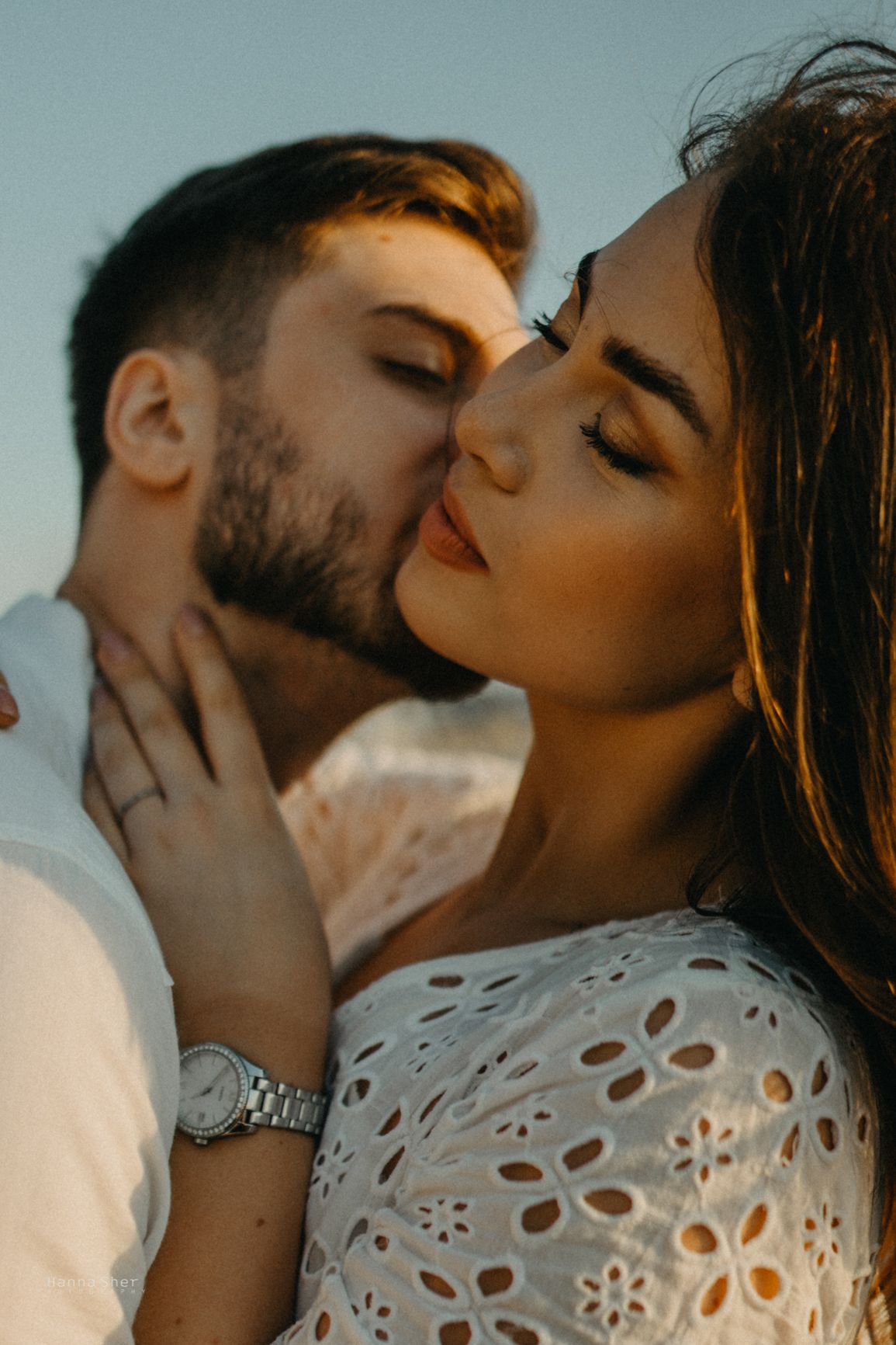 Couple sharing an intimate moment at sunset, man kissing womans cheek during engagement session.