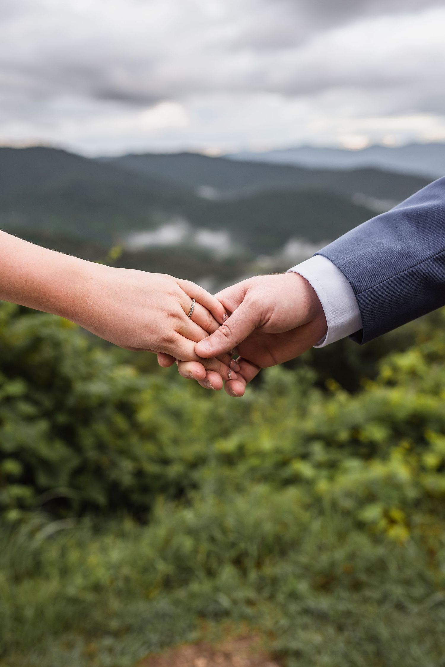 Close up of two hands holding with mountains behind during Blue Ridge Parkway photoshoot.