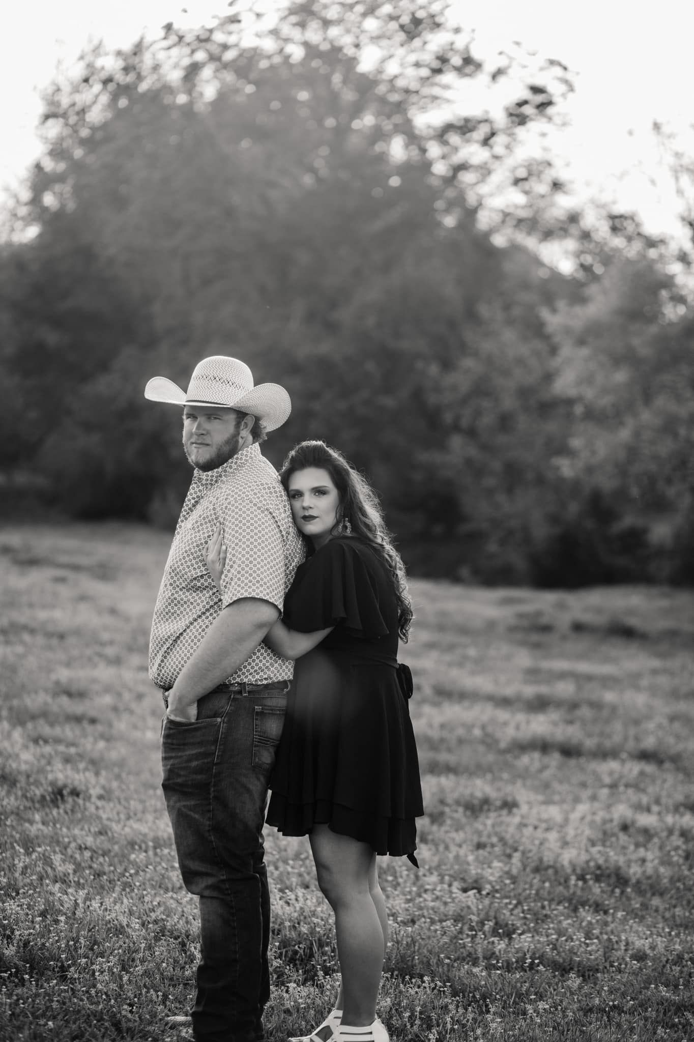 Black and white portrait of couple embracing in a sunlit meadow with rustic country style.