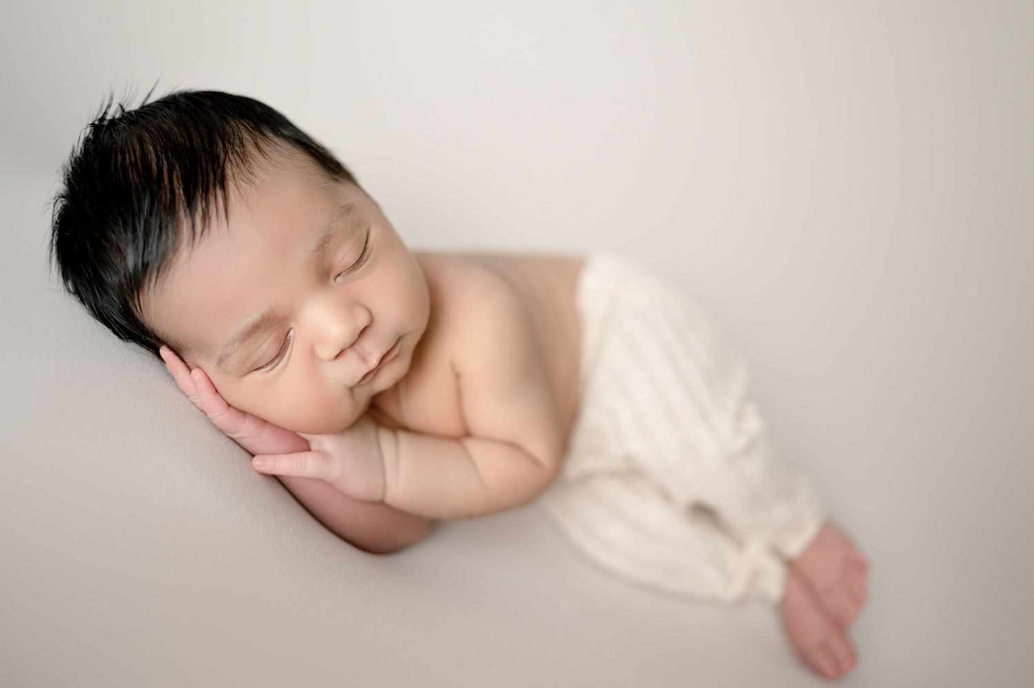 Newborn baby sleeping peacefully on soft white surface.