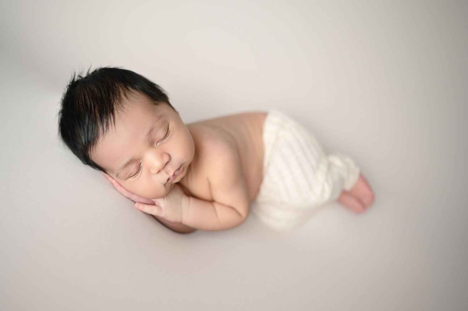 Sleeping baby in white wrap on neutral backdrop.