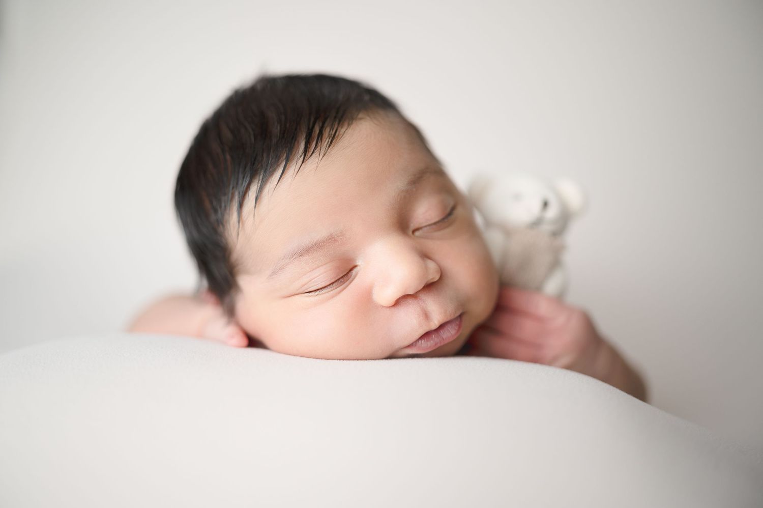 Side profile of a sleeping newborn wrapped in white fabric against neutral backdrop.