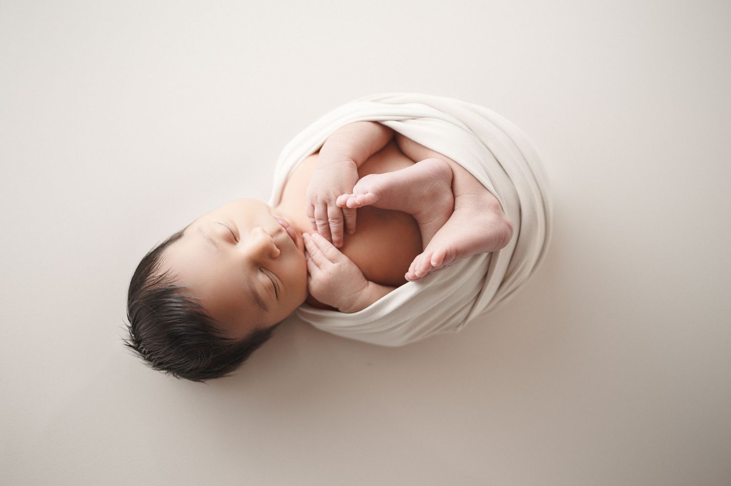 Artistic overhead view of a newborn wrapped in soft fabric against white background.