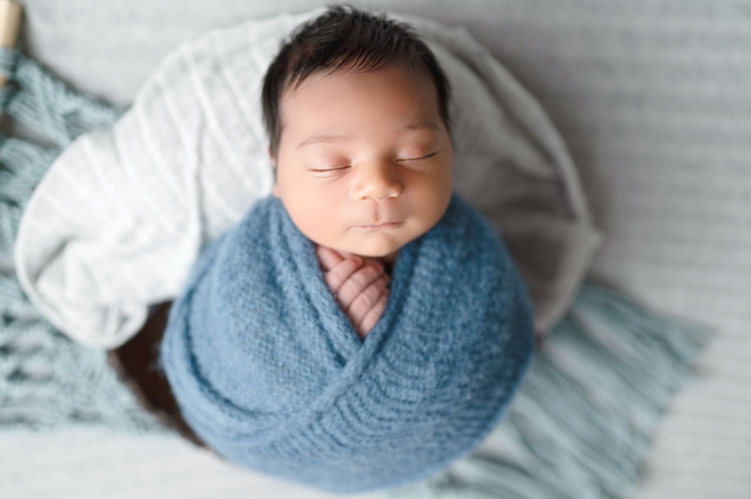 Professional newborn photos showing sleeping baby wrapped in blue swaddle on light backdrop.
