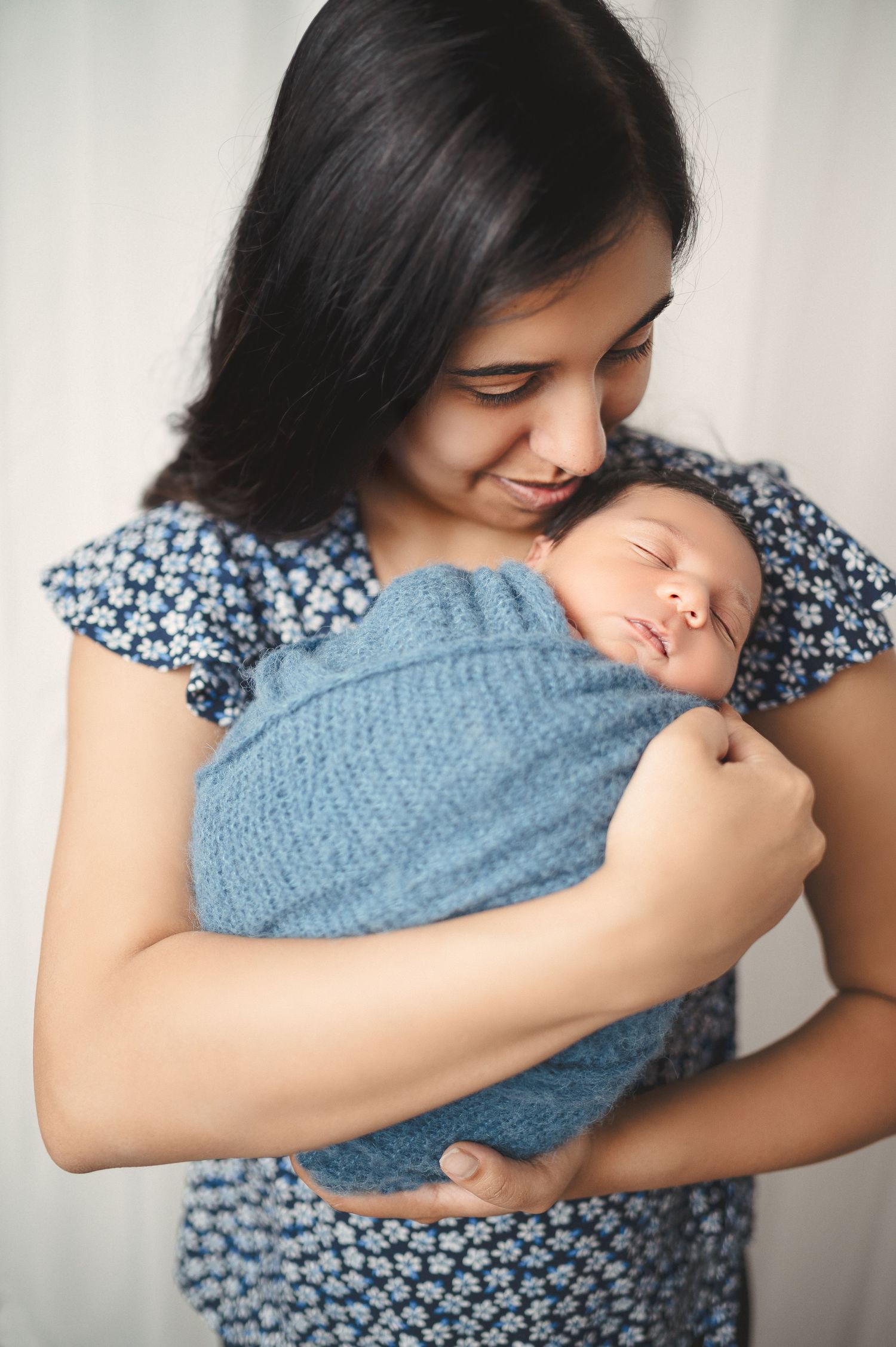 Loving family portrait series with mother holding newborn wrapped in blue knit blanket.