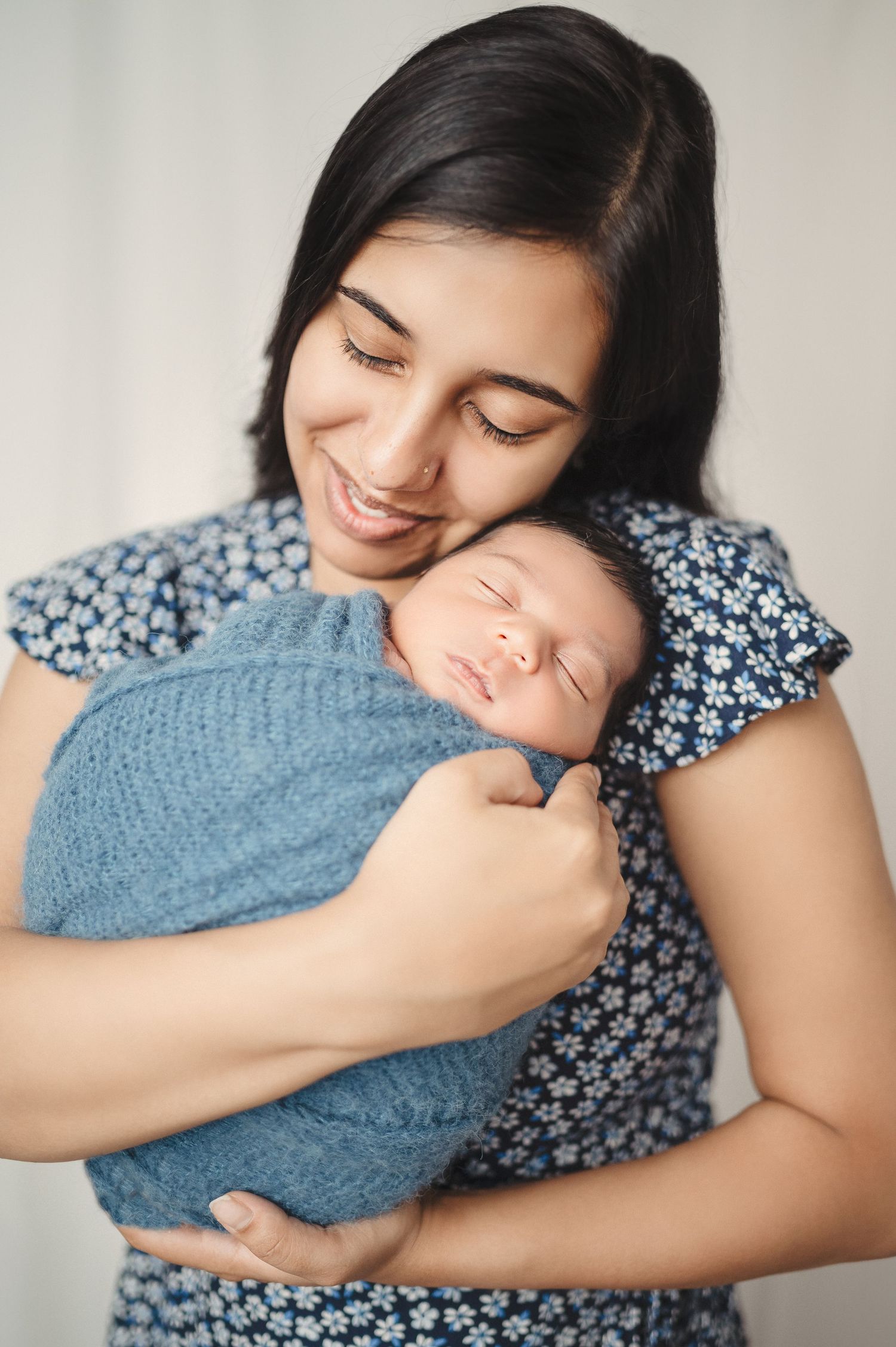 Sweet candid moments of mother embracing newborn baby swaddled in soft blue wrap.