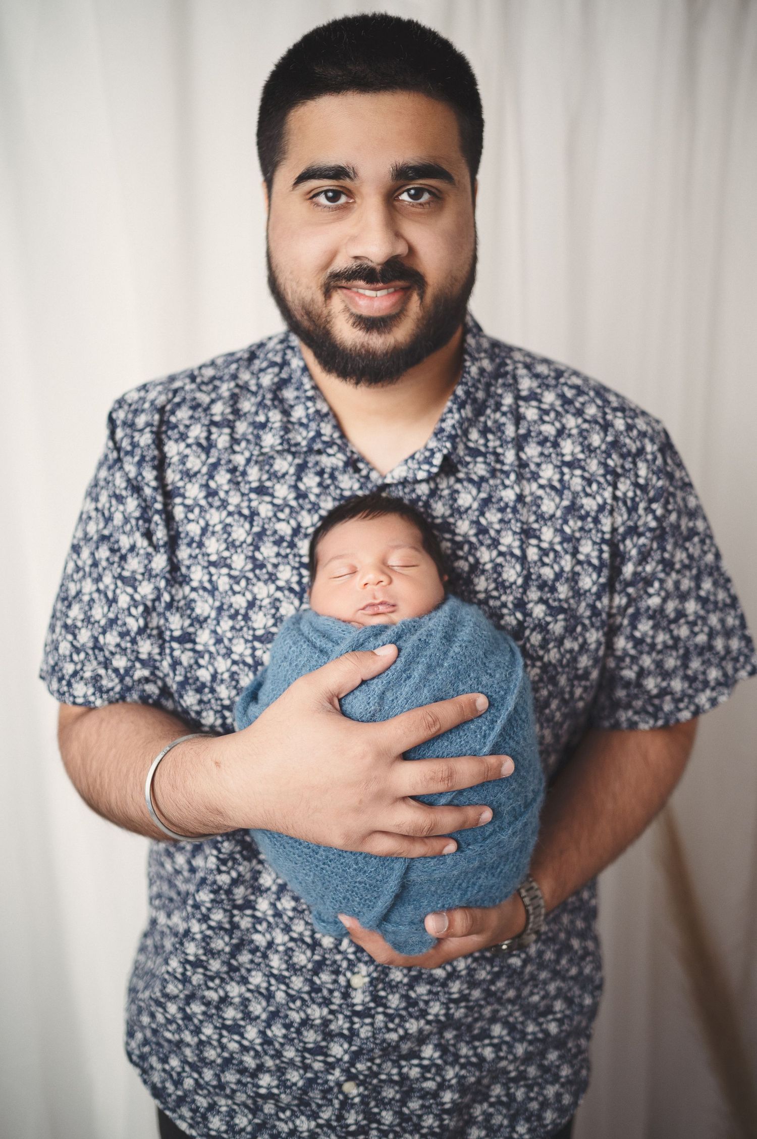 A parent wearing a patterned shirt cradles their sleeping newborn wrapped in blue fabric.