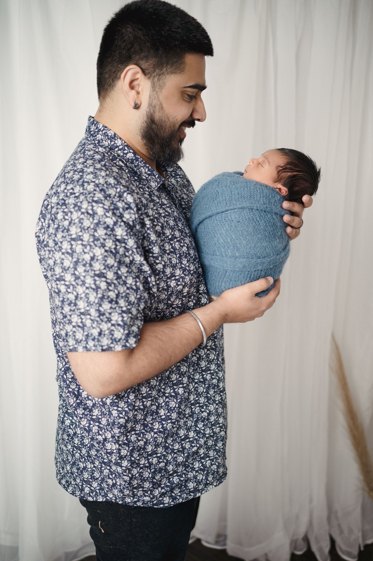A parent in profile view holds their swaddled newborn against a light curtain background.