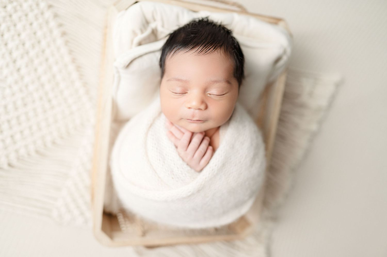 Sleeping newborn baby swaddled in white blanket during professional photo session.