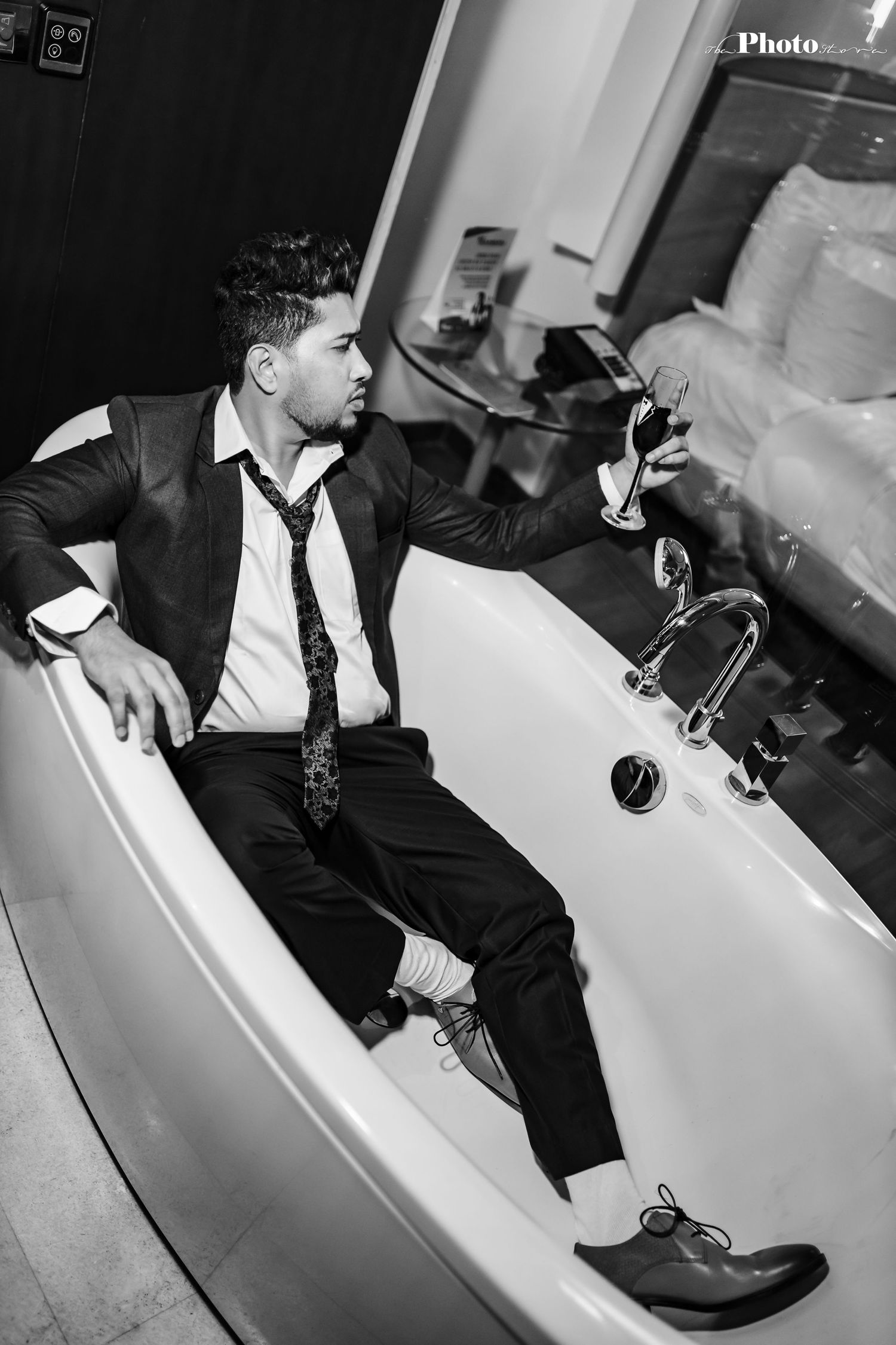 Person in formal attire lounging in a white bathtub during a stylized photoshoot.