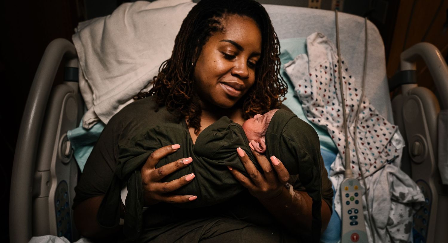 Woman Smiling While Holding Newborn In Hands Sitting On Hospital Bed
