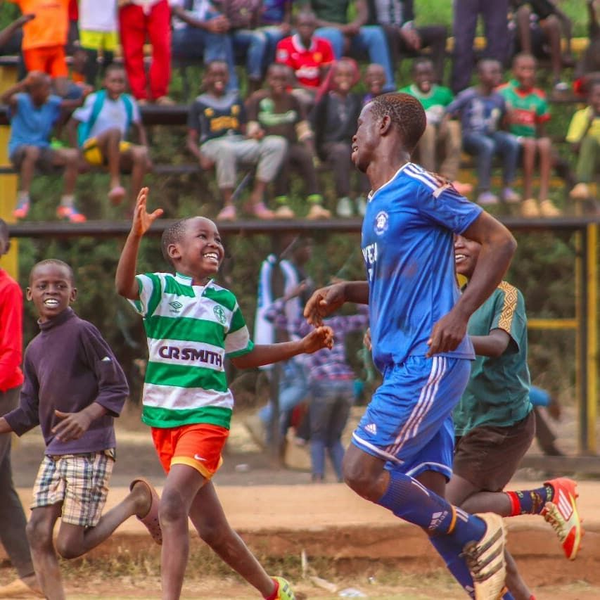 a young boy rushng to a soccer/football player to congratulate him on scoring a goal