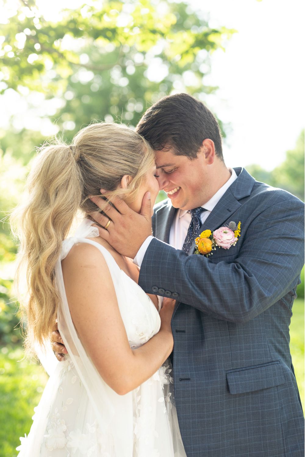 Intimate wedding moment captured in natural sunlight with blue suit and white dress.