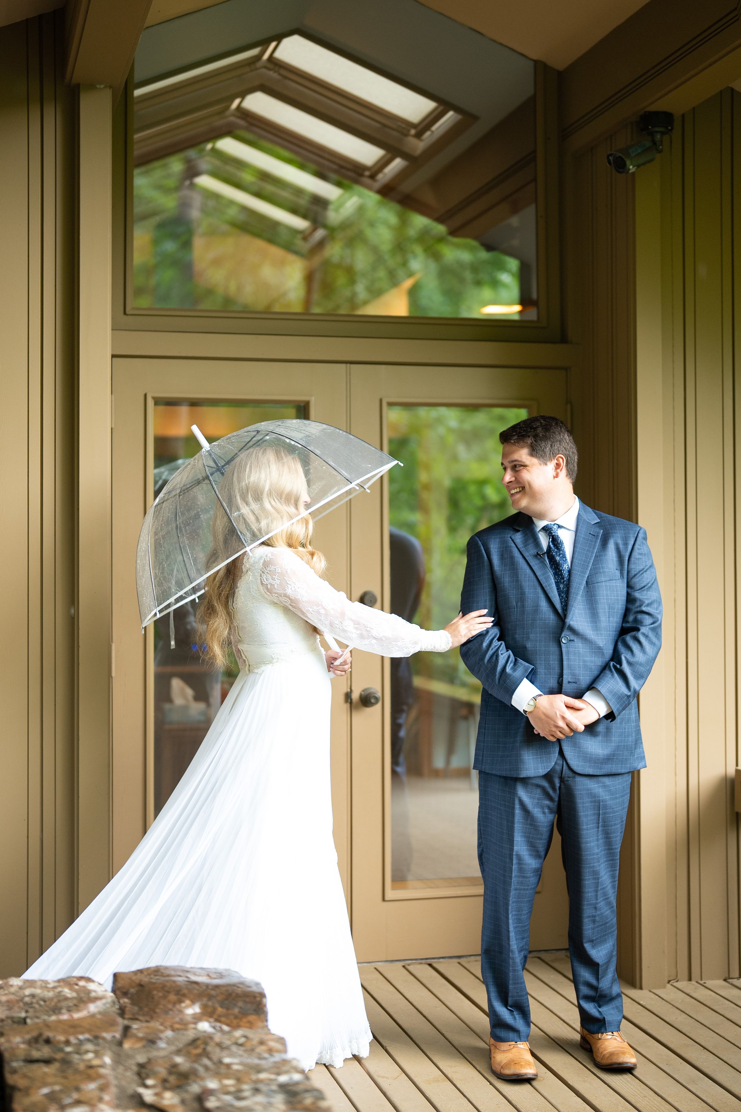 Wedding couple in navy suit and white dress posing playfully in wooden gazebo.