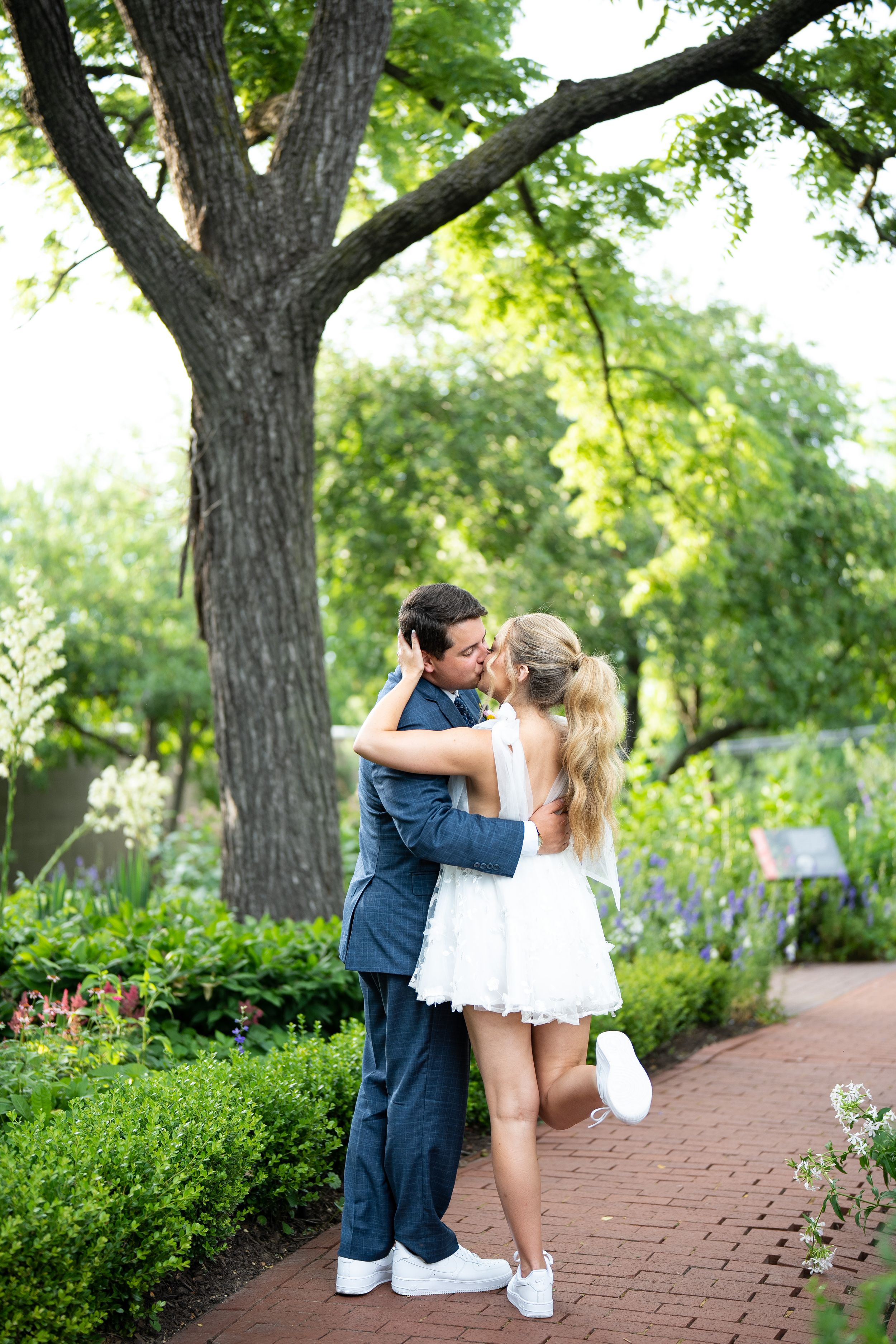 Wedding couple embracing on a brick pathway in a lush garden setting.