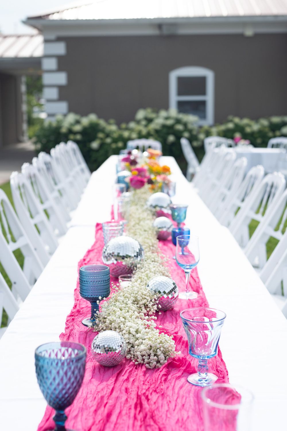 Wedding reception setup with white chairs and pink decor featuring baby's breath floral arrangements.
