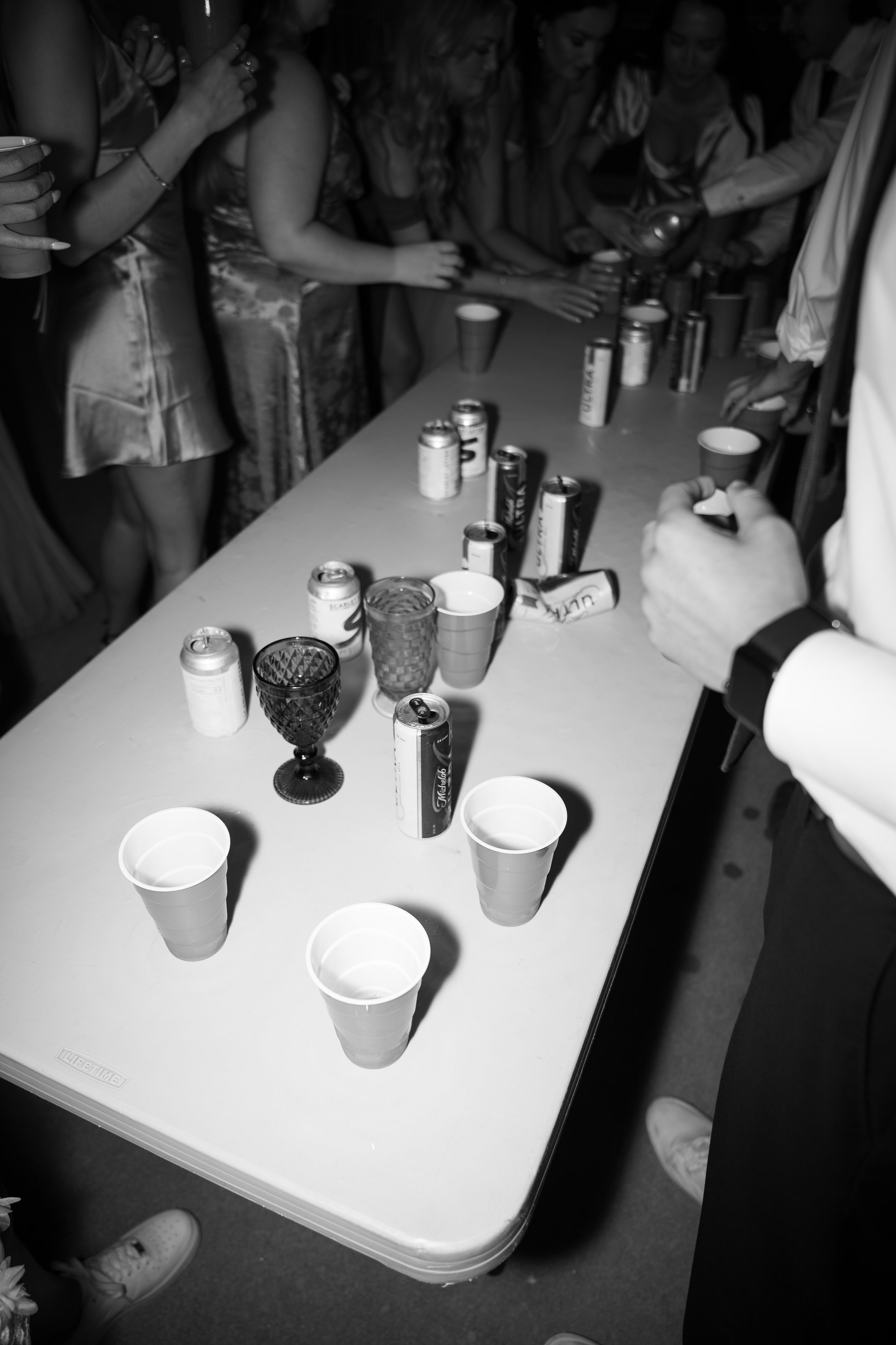 Black and white photo of drinks and glassware arranged on a white table at an event.