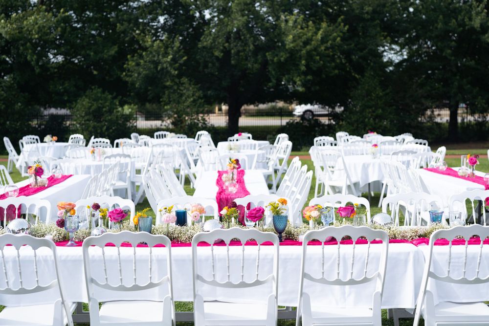 Outdoor wedding venue with rows of white folding chairs and pink table settings.