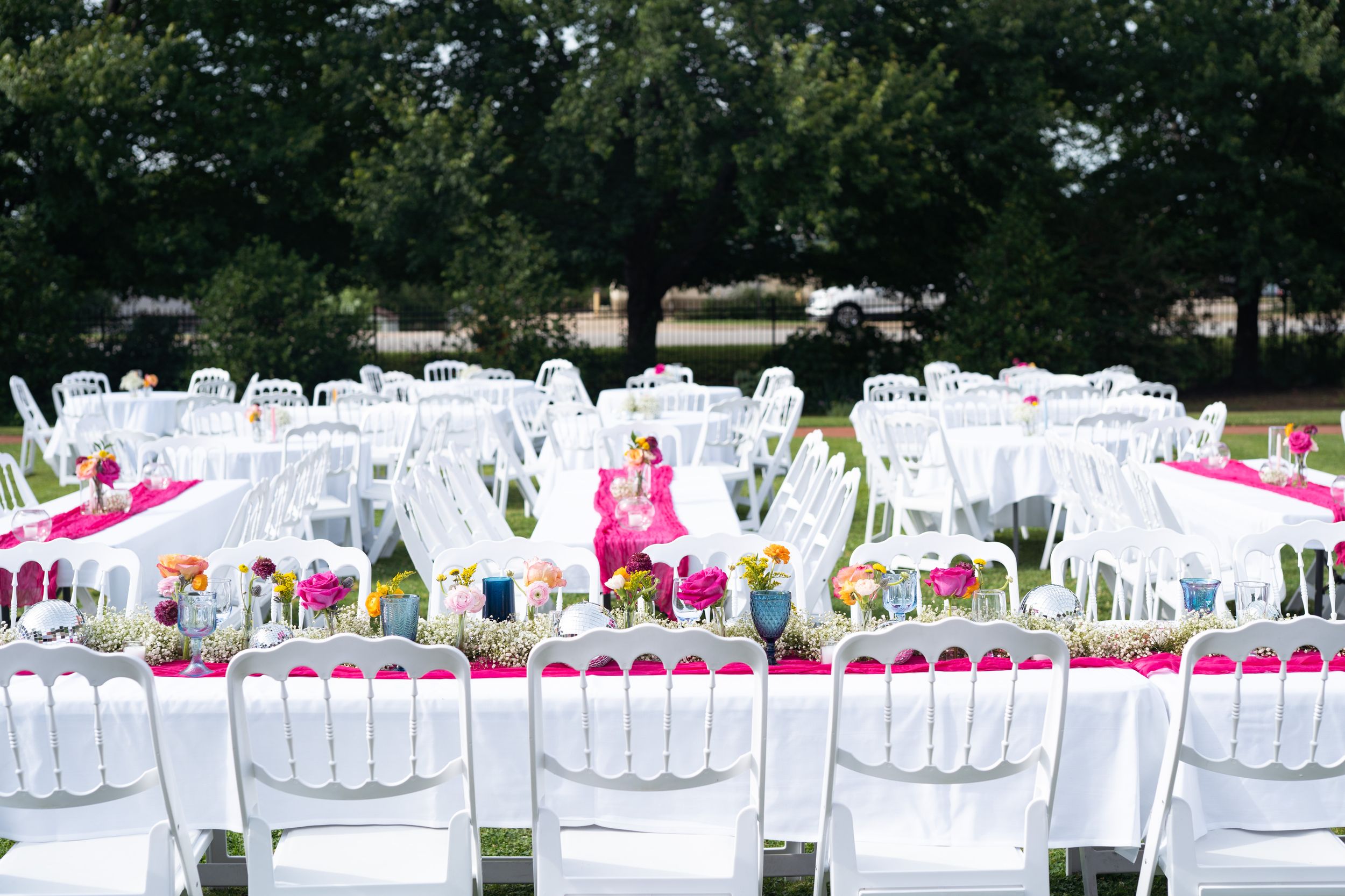 Outdoor wedding venue with rows of white folding chairs and pink table settings.