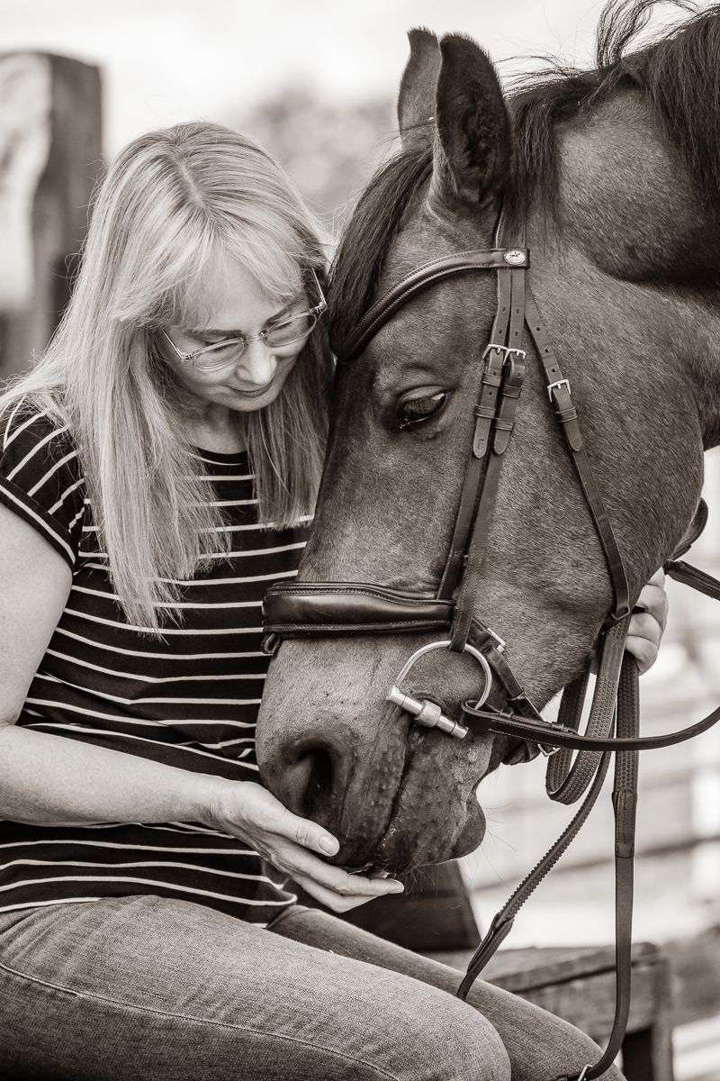 An intimate black and white moment showing a gentle connection between a horse and someone in casual attire.