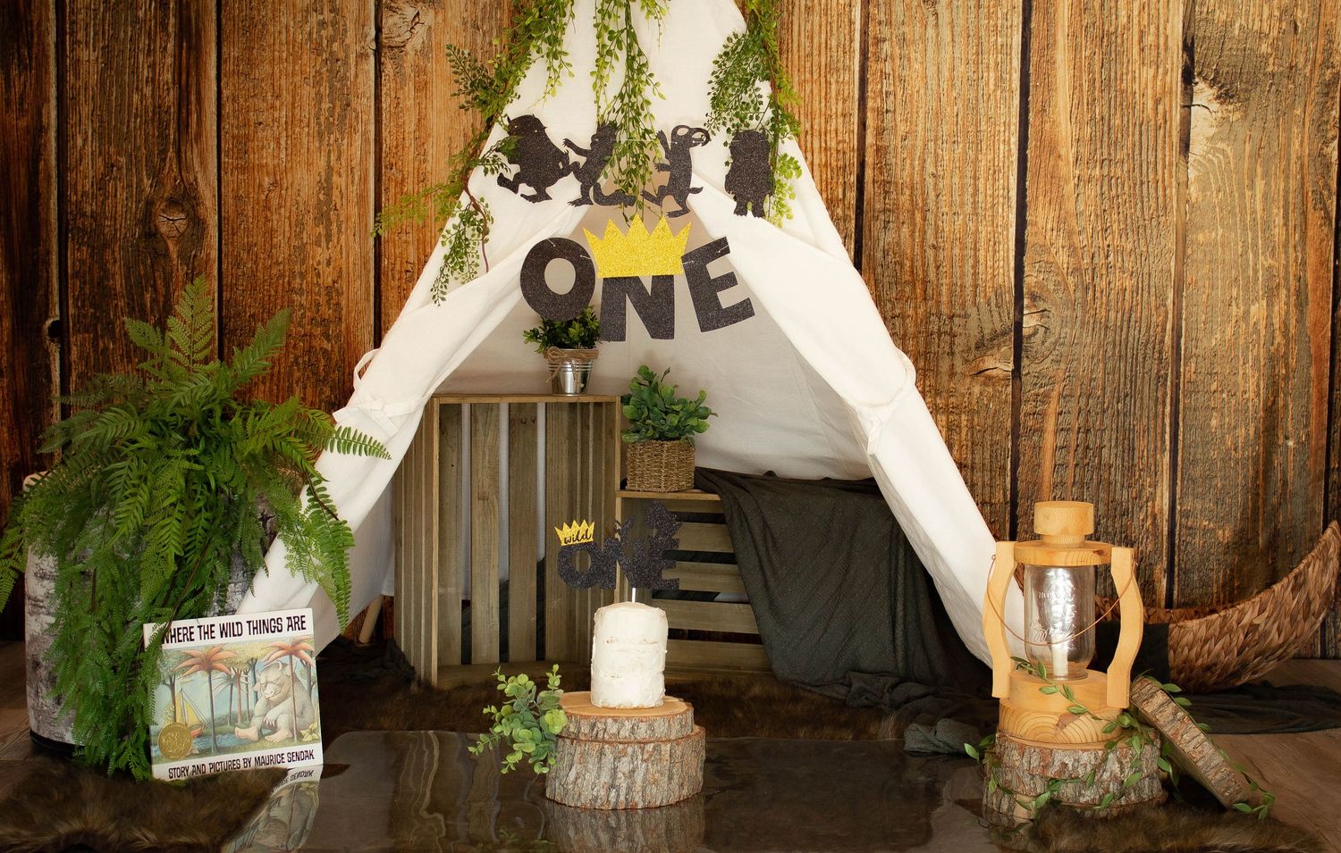 Rustic woodland-themed teepee photo setup with greenery and 'ONE' text decoration.