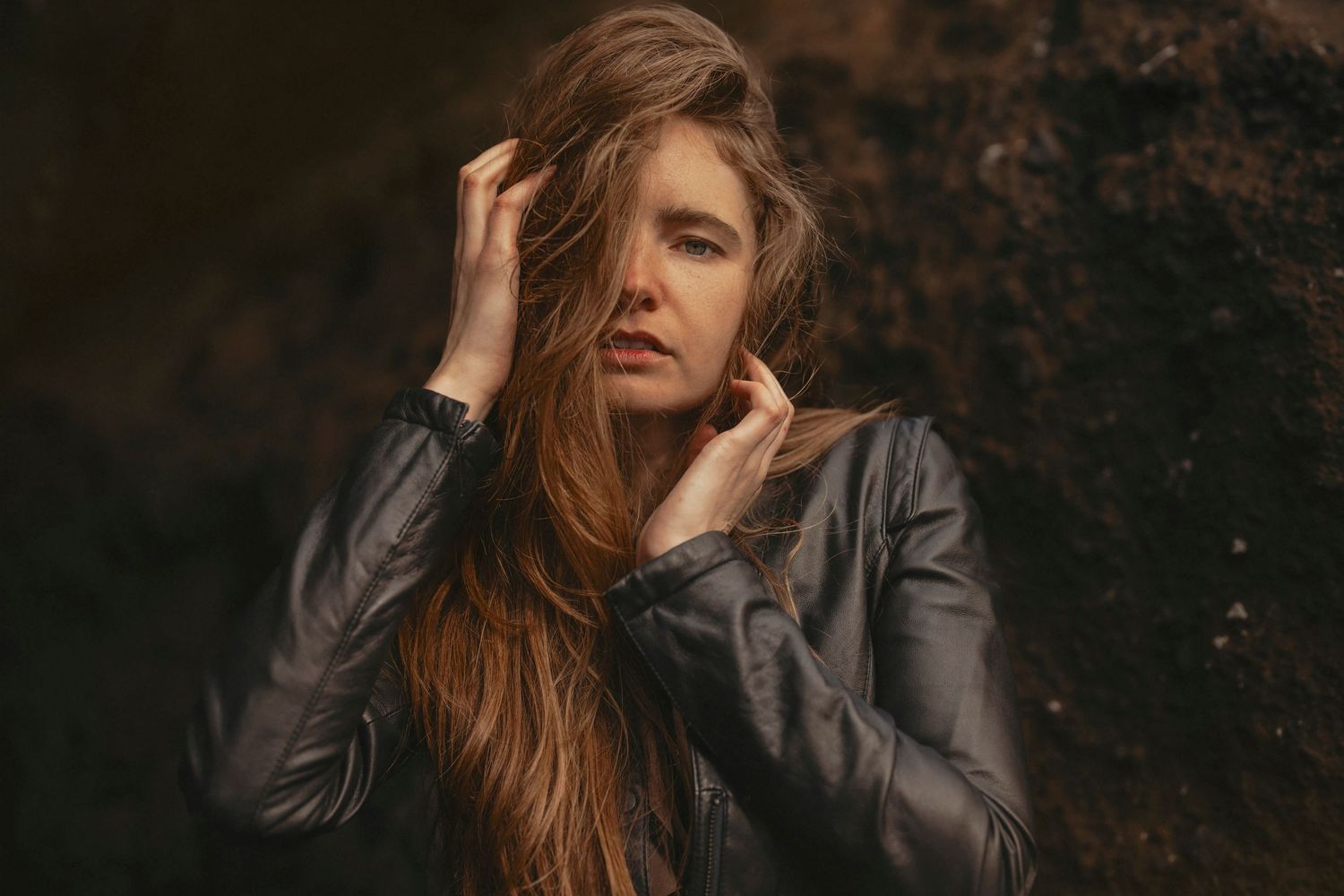 A moody portrait against a dark textured background with dramatic lighting.