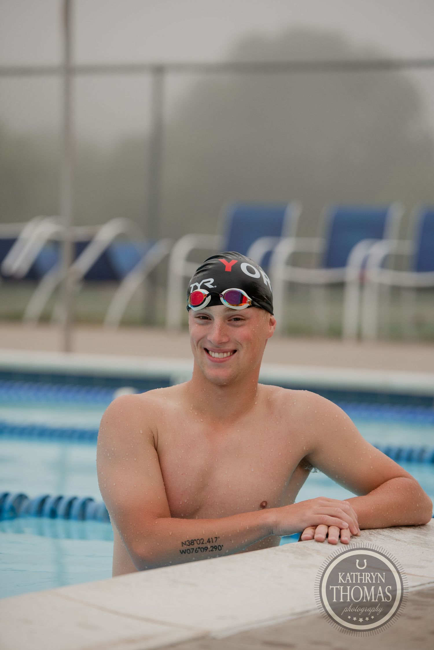 A competitive swimmer in goggles and swim cap poses at poolside.
