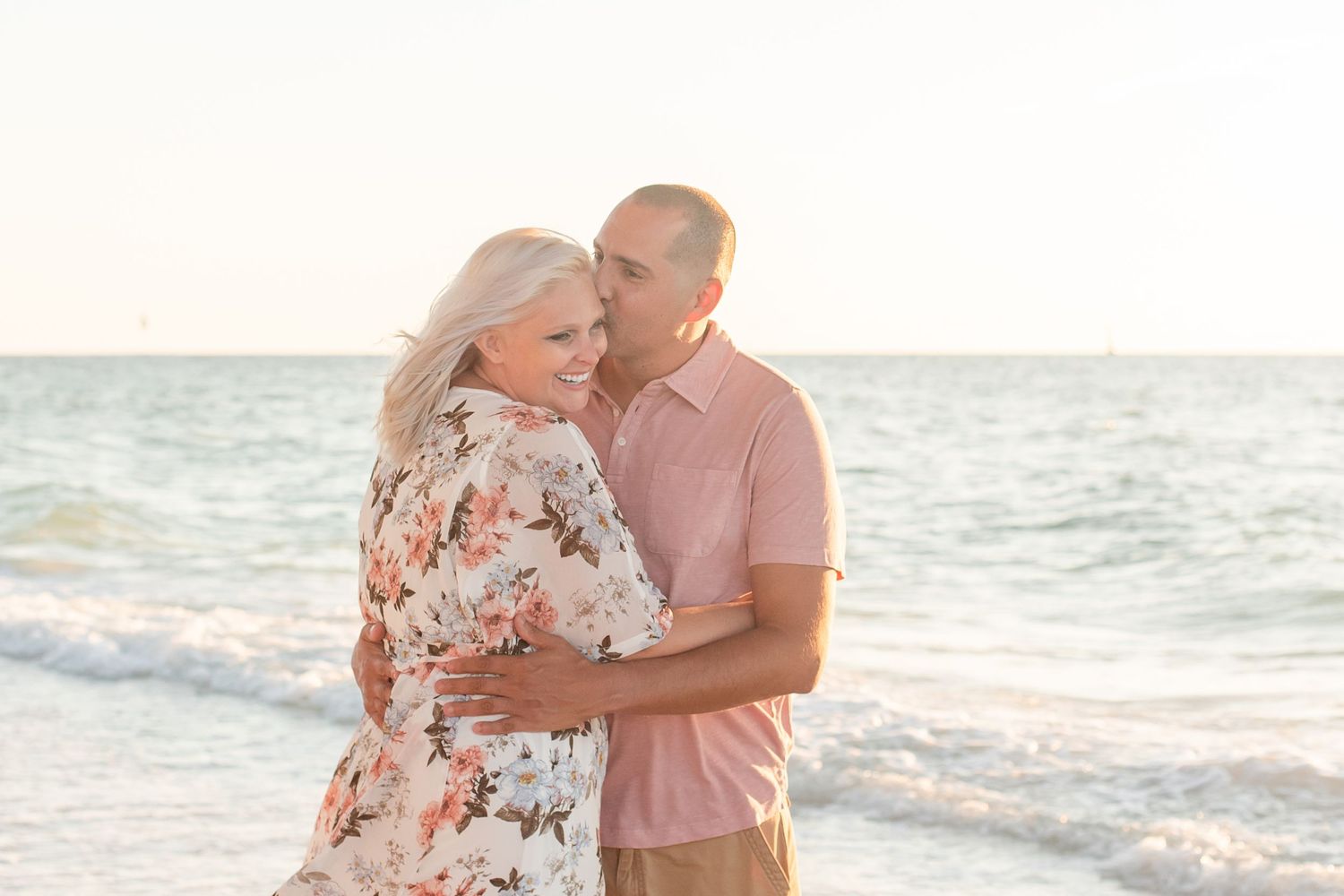 Couple in coordinated pink and floral outfits sharing tender moments by the ocean.