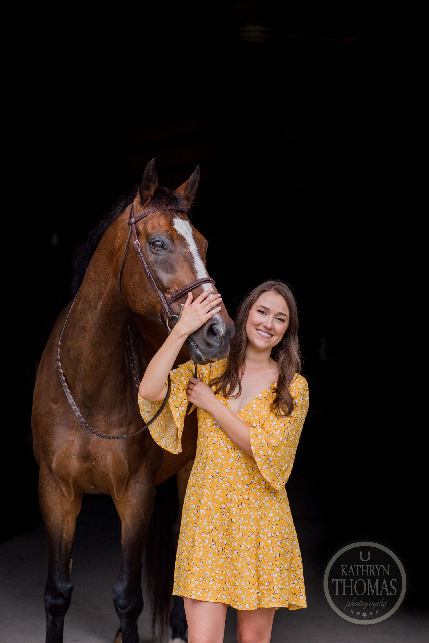 A dramatic indoor portrait of a bay horse and person in yellow dress against black background.